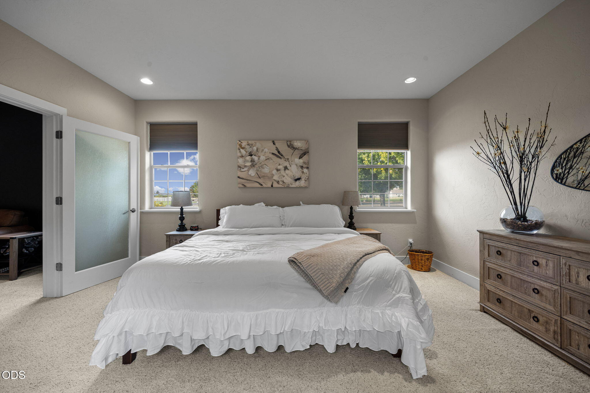 Furnished bedroom with a white bed, two windows, floral wall art, and a wooden dresser.