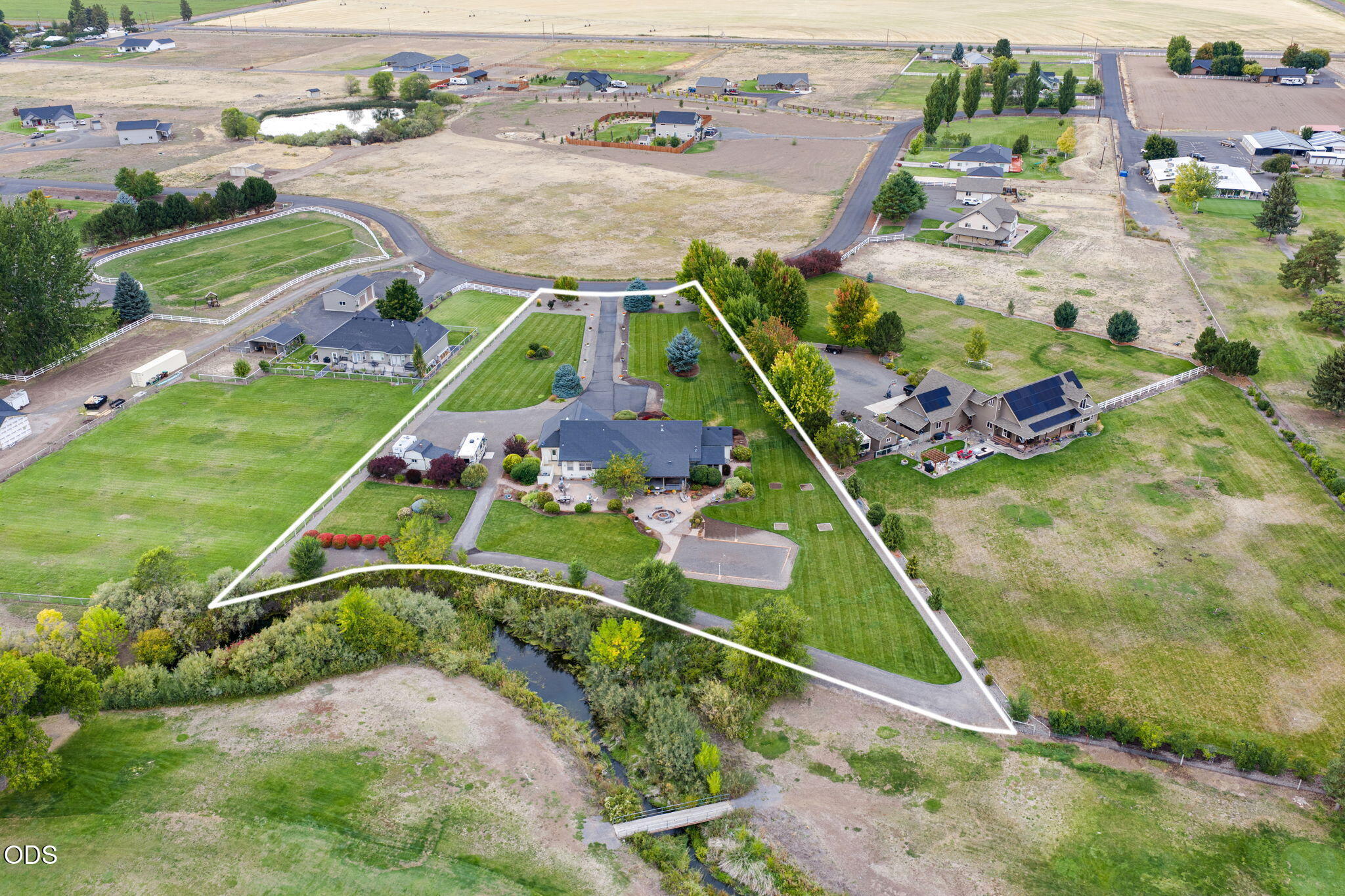 Aerial view of a rural home and landscaped lot outlined beside a creek.