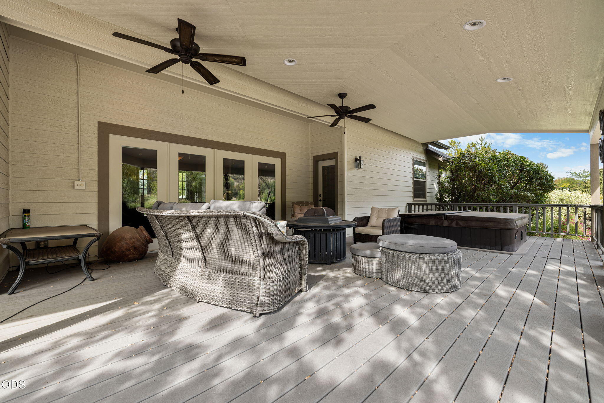 Covered deck with wicker lounge seating, ceiling fans, and a hot tub beside the house.