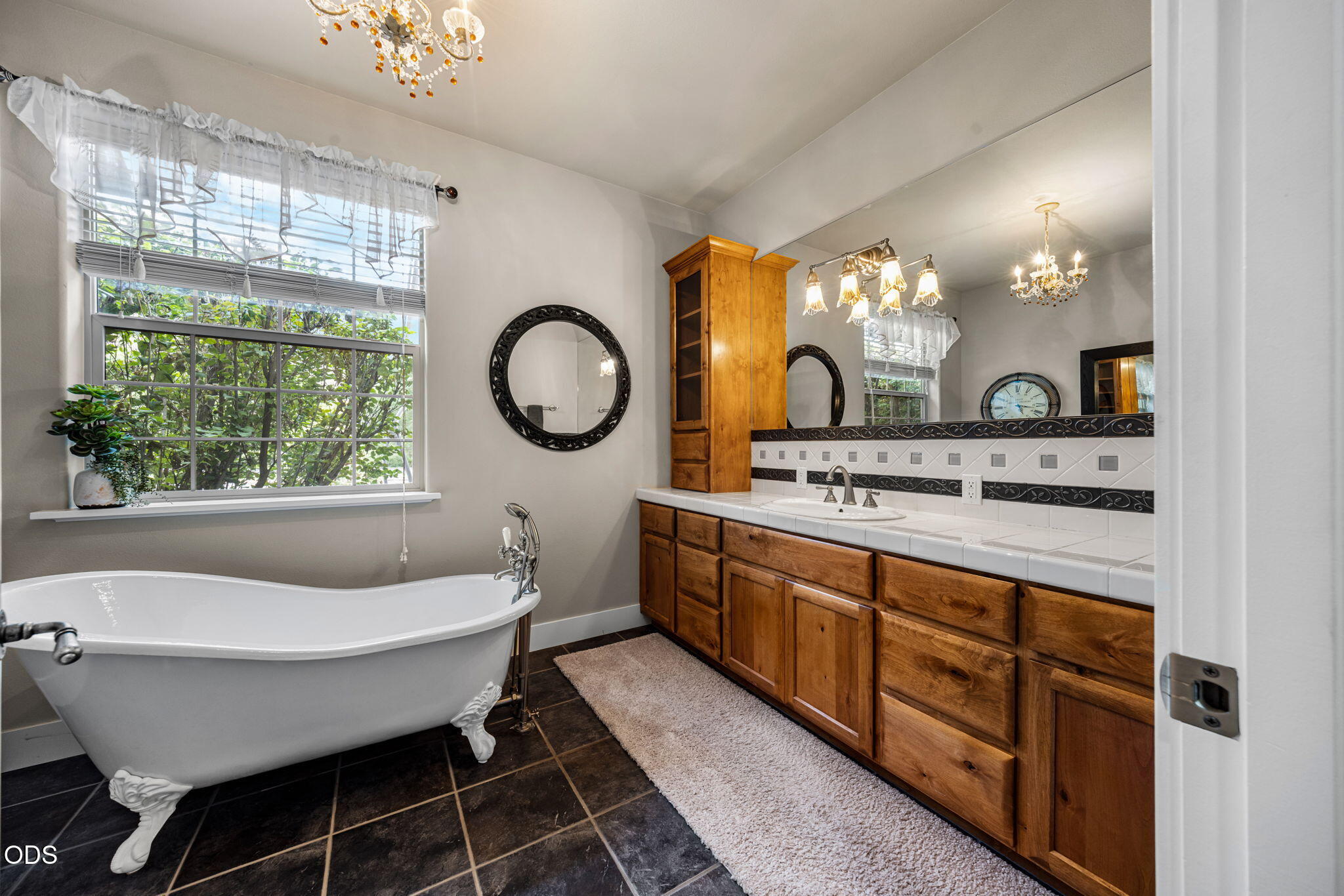 Bathroom with a clawfoot tub, wood vanity, and large window overlooking greenery.