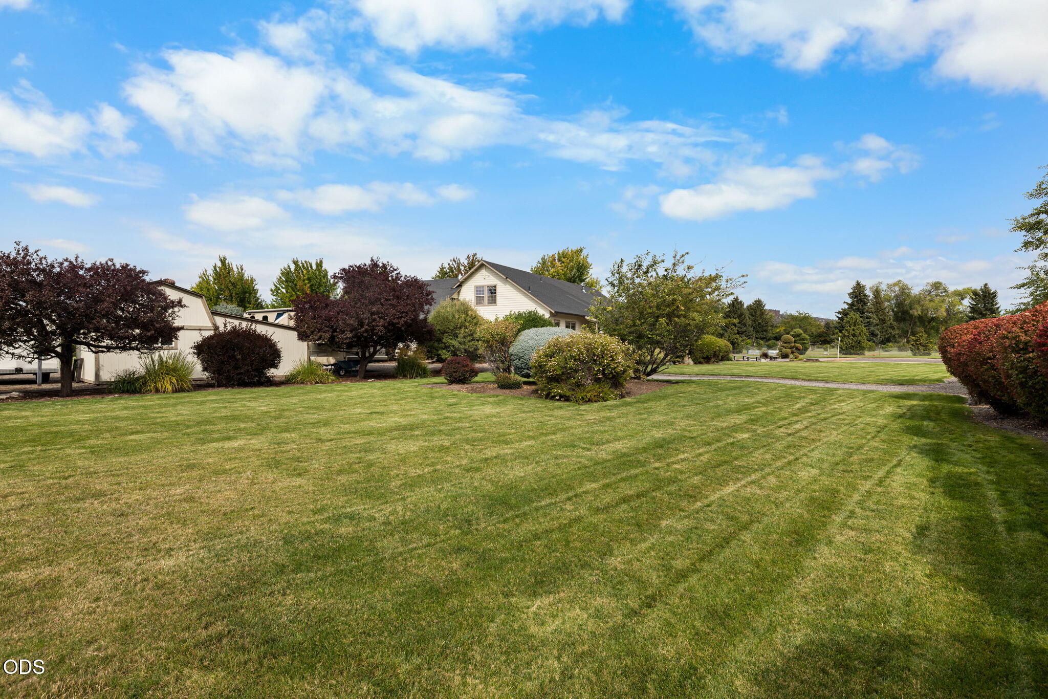 Light-colored house partly screened by trees behind a broad mowed lawn.