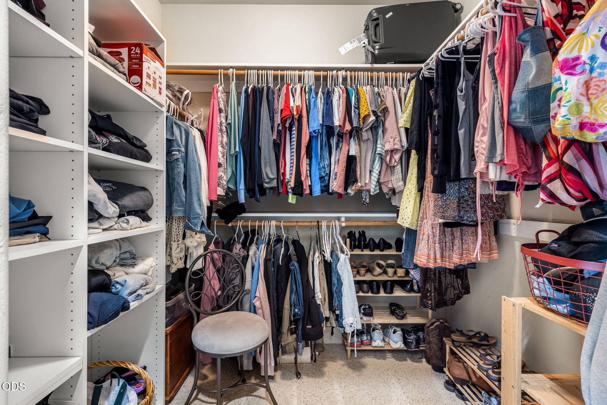 Walk-in closet with built-in shelves, two levels of hanging clothes, and shoes arranged along the back wall.