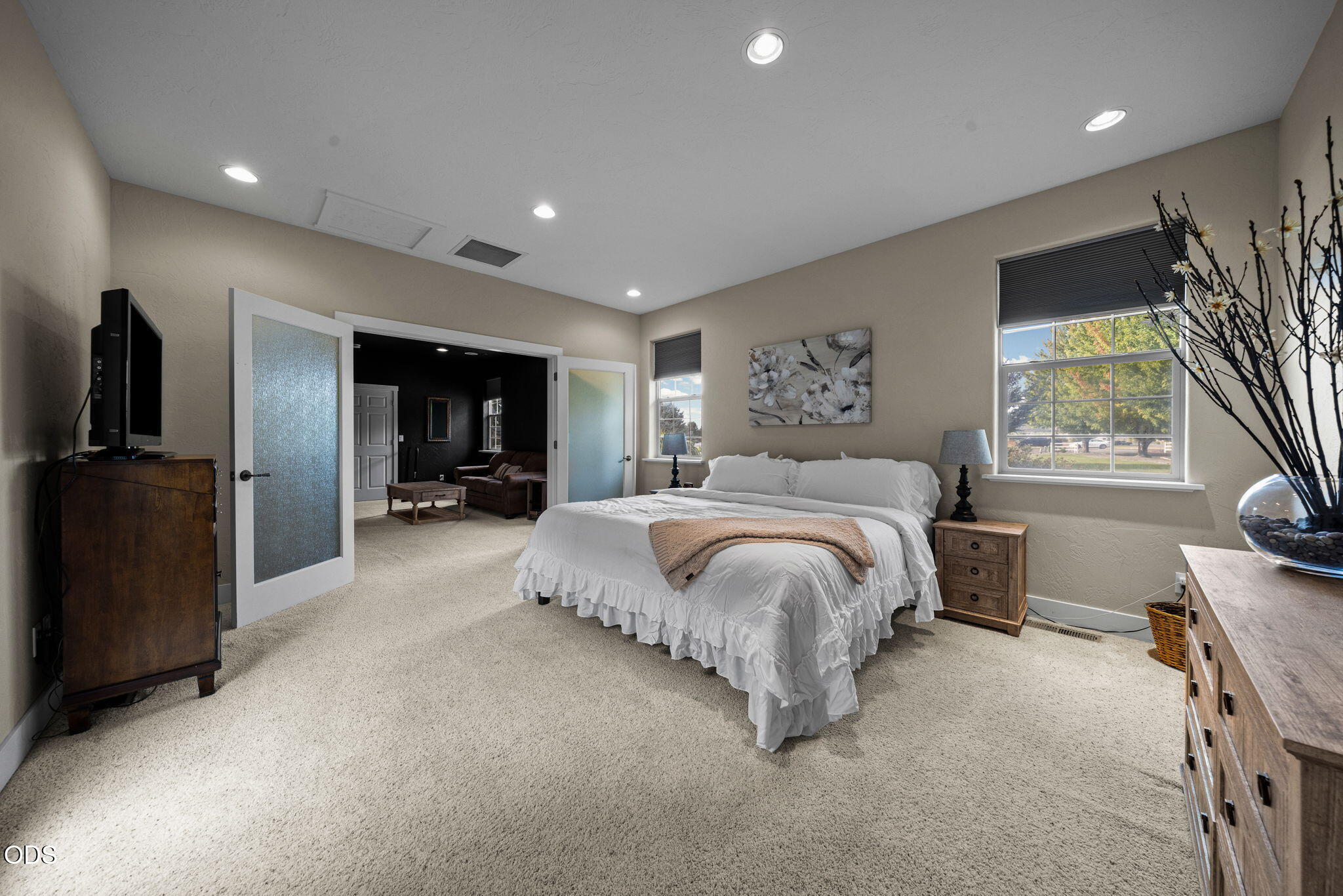 Staged bedroom with a white bed, carpet, and open doors to an adjoining sitting room.