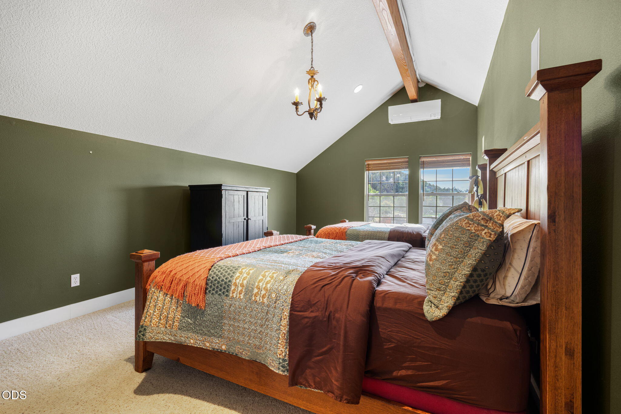 Bedroom with two wooden beds, patterned quilts, and a vaulted ceiling with an exposed beam.