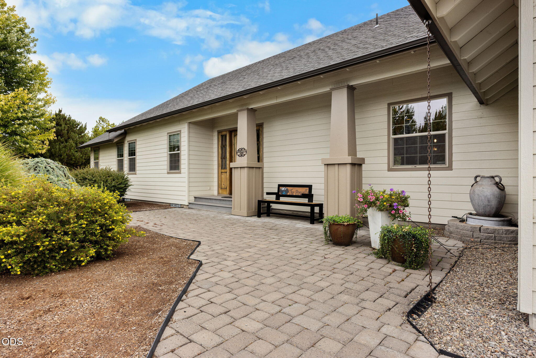 House exterior with a covered porch, paved patio, potted flowers, and a hanging rain chain.