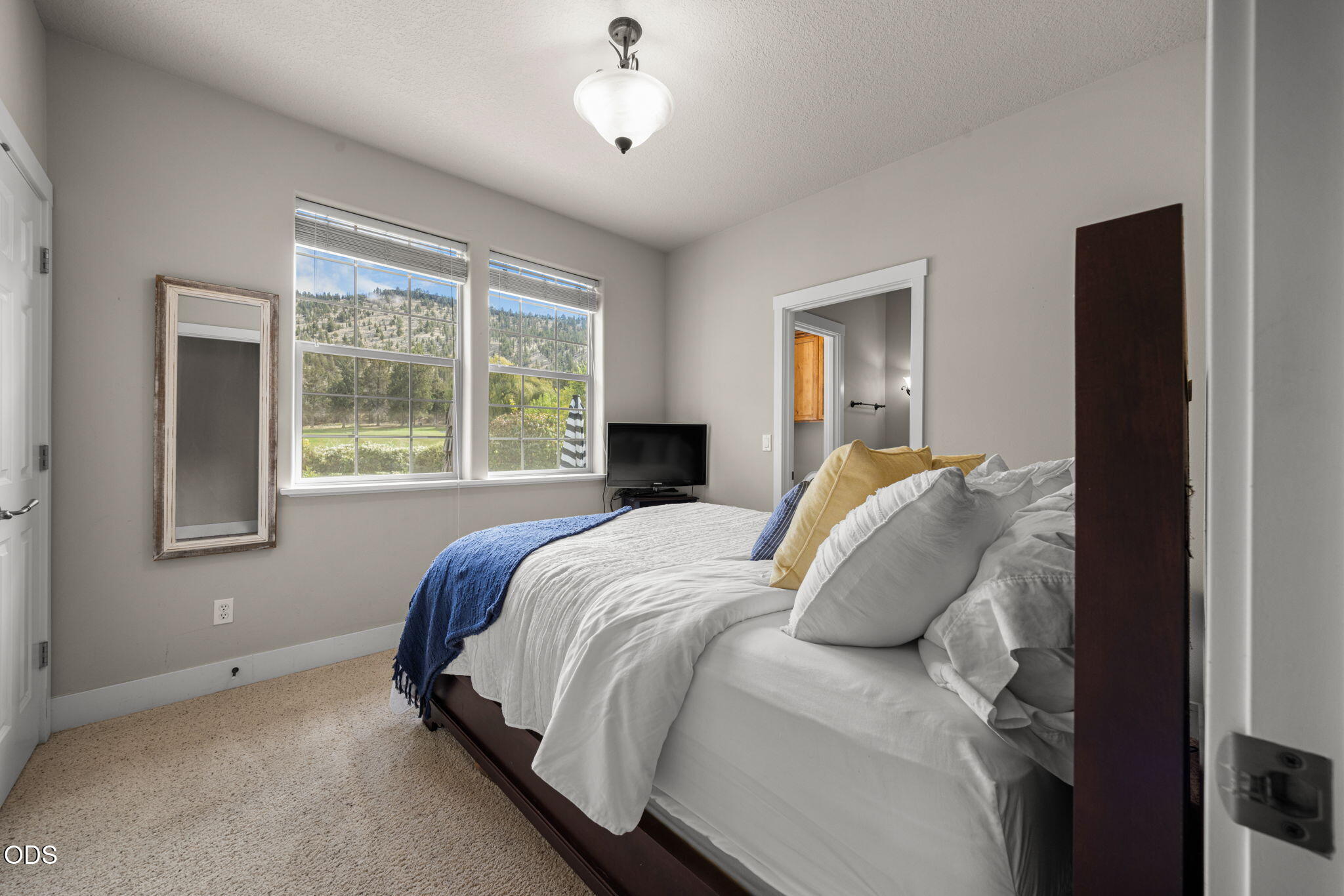 Bedroom with a white bed, blue throw, and windows overlooking wooded hills.