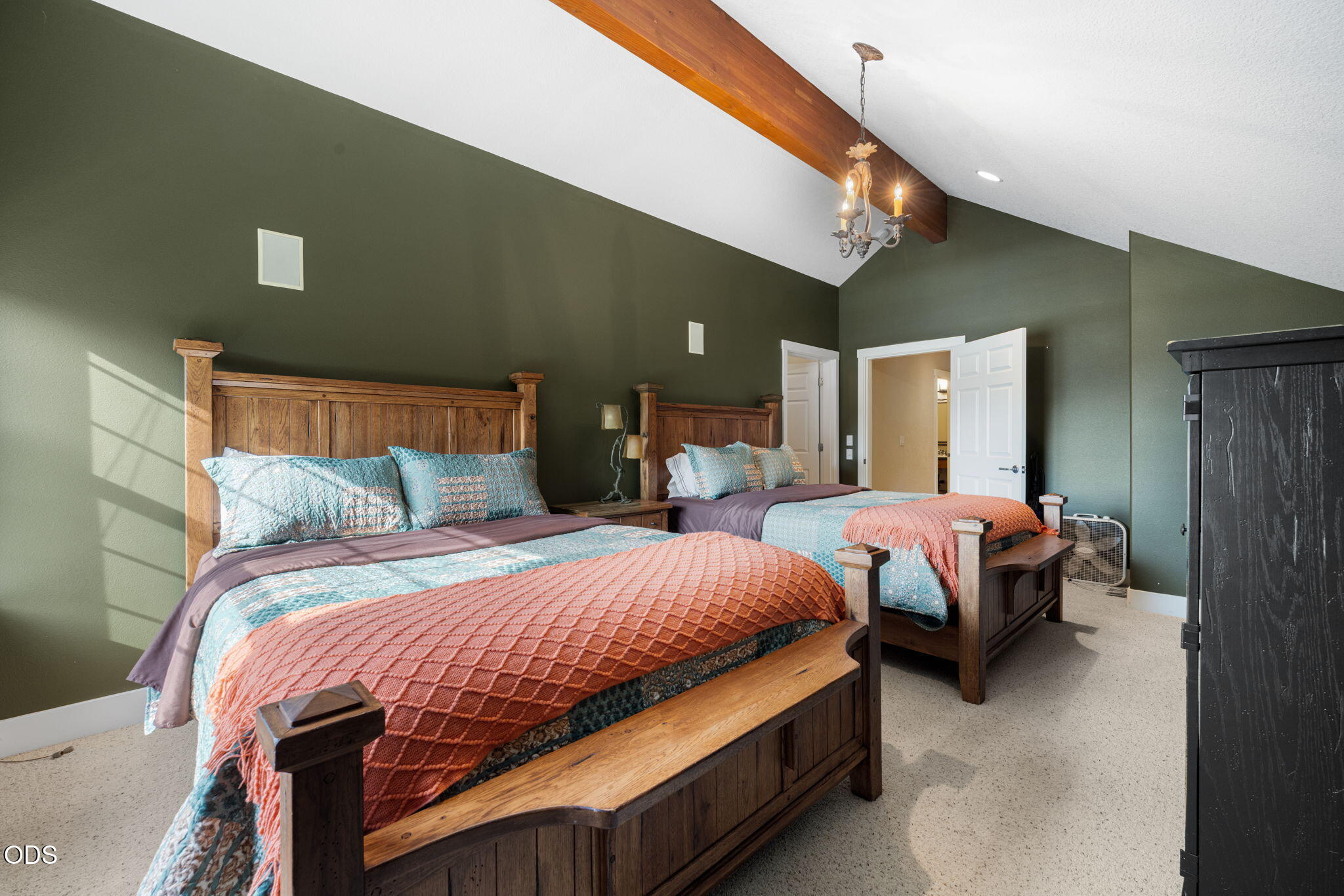 Bedroom with two rustic wooden beds, colorful bedding, and a vaulted ceiling with an exposed beam.