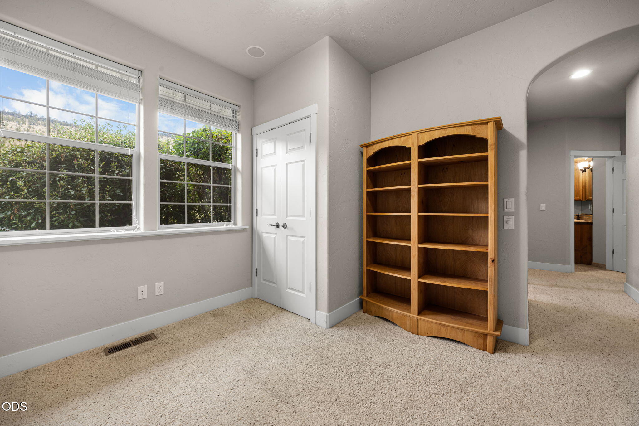 Carpeted room with large windows, double closet doors, and a tall wooden bookcase.
