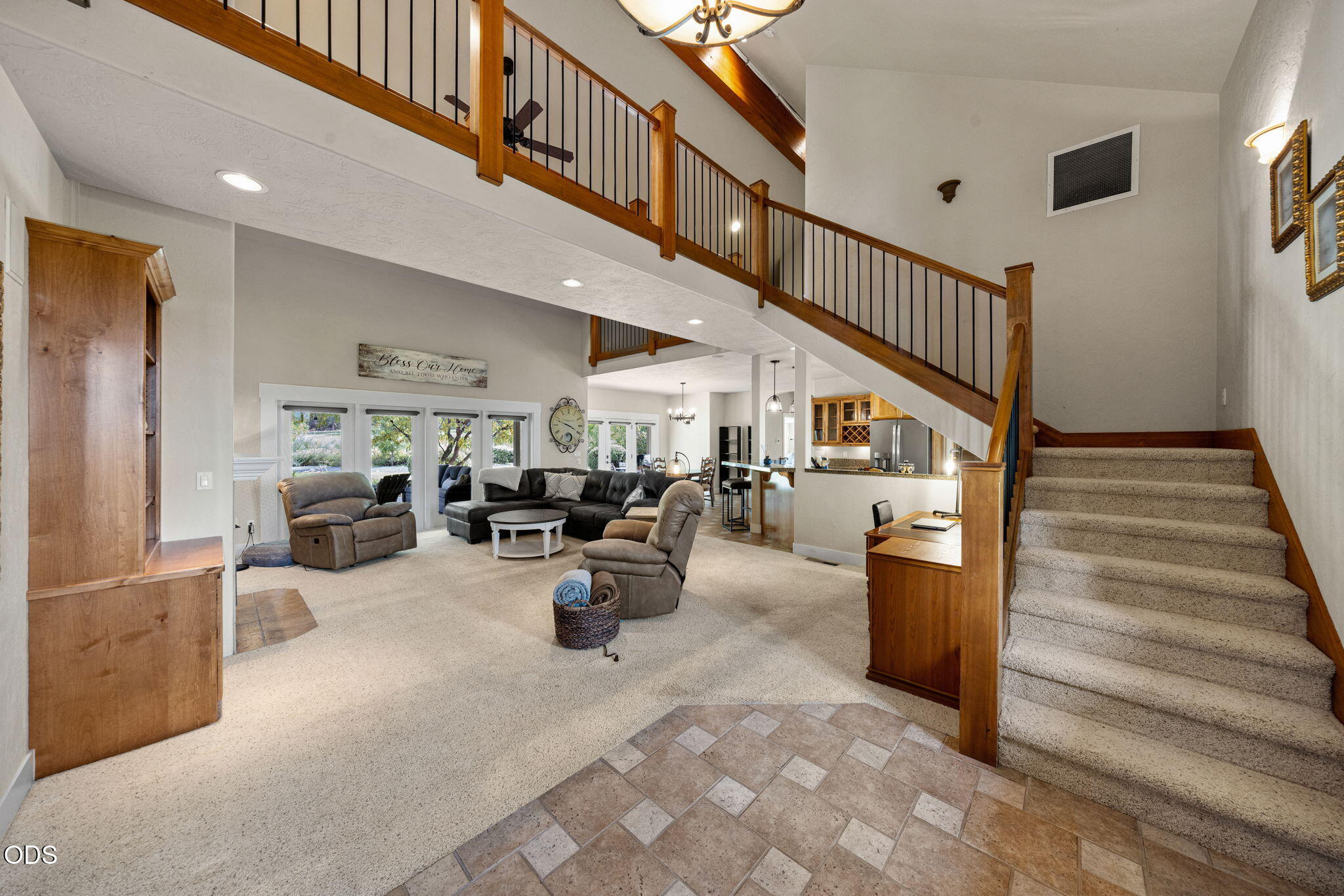 Open living room with leather seating, large windows, and a staircase leading to an upstairs loft.