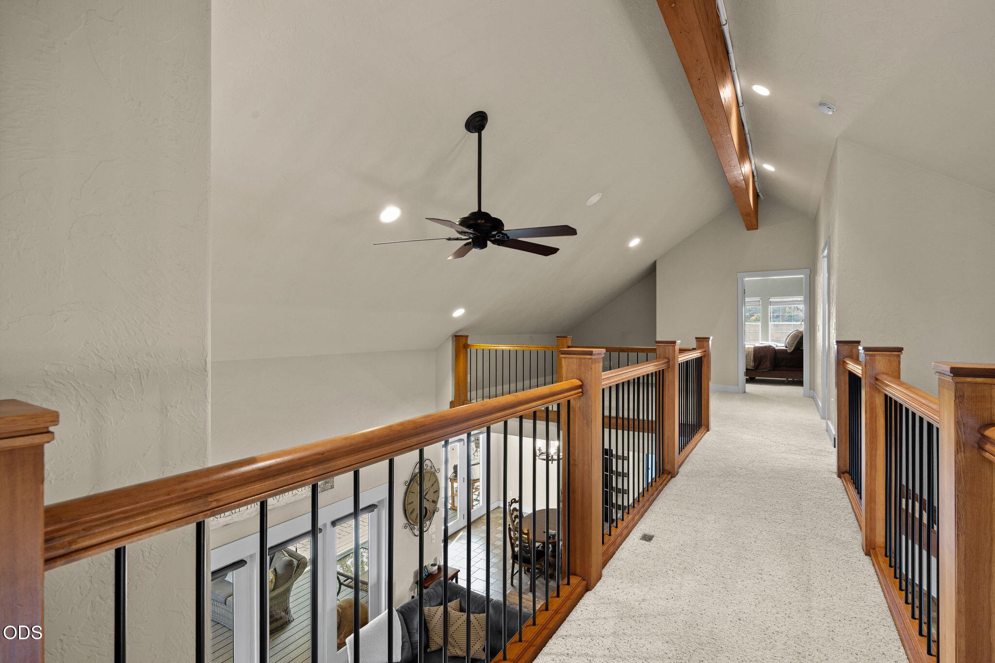 Upstairs loft landing with wood-and-metal railings, vaulted ceiling, and ceiling fan.