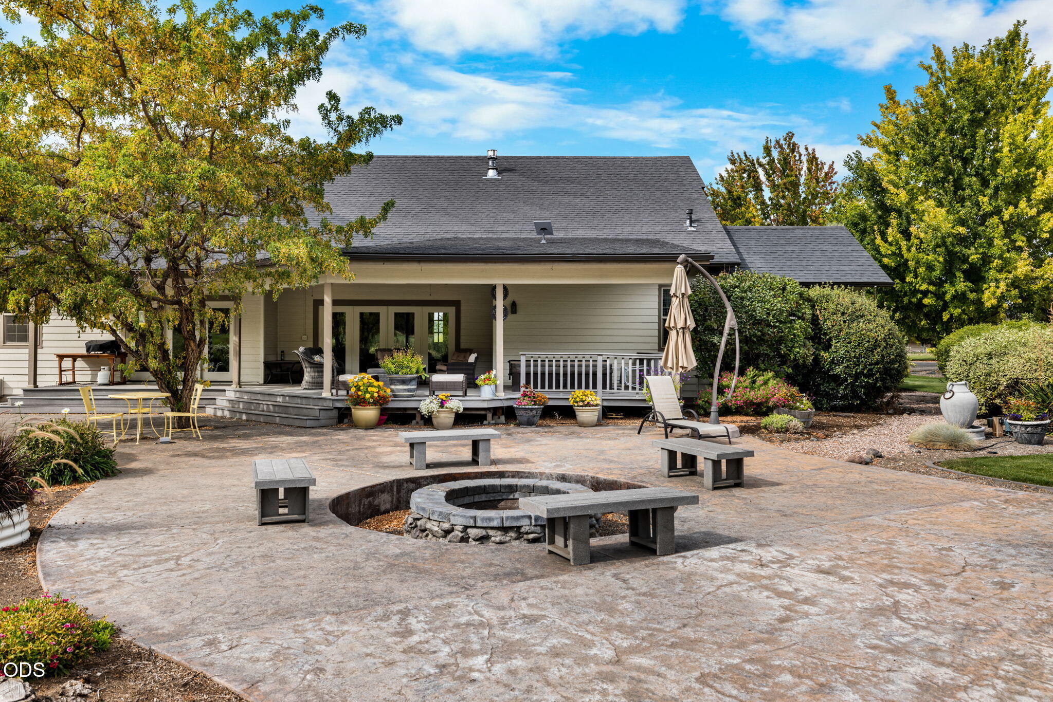 Home’s covered rear deck and landscaped patio with a circular fire pit and benches.