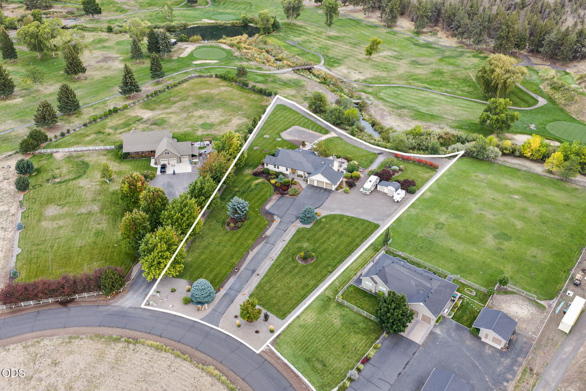 Aerial view of a home with landscaped grounds, outbuildings, and a white boundary line beside a golf course.