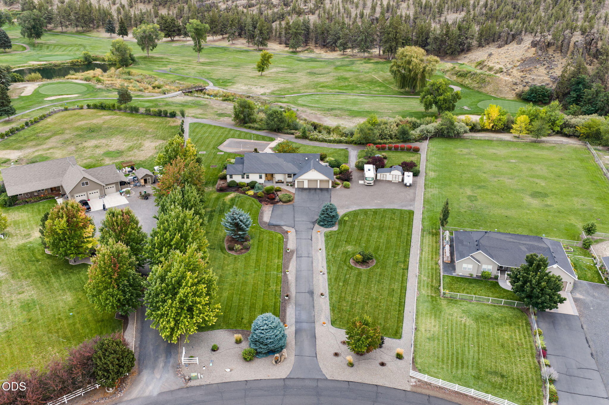 Aerial view of a landscaped home with a long driveway beside a golf course.