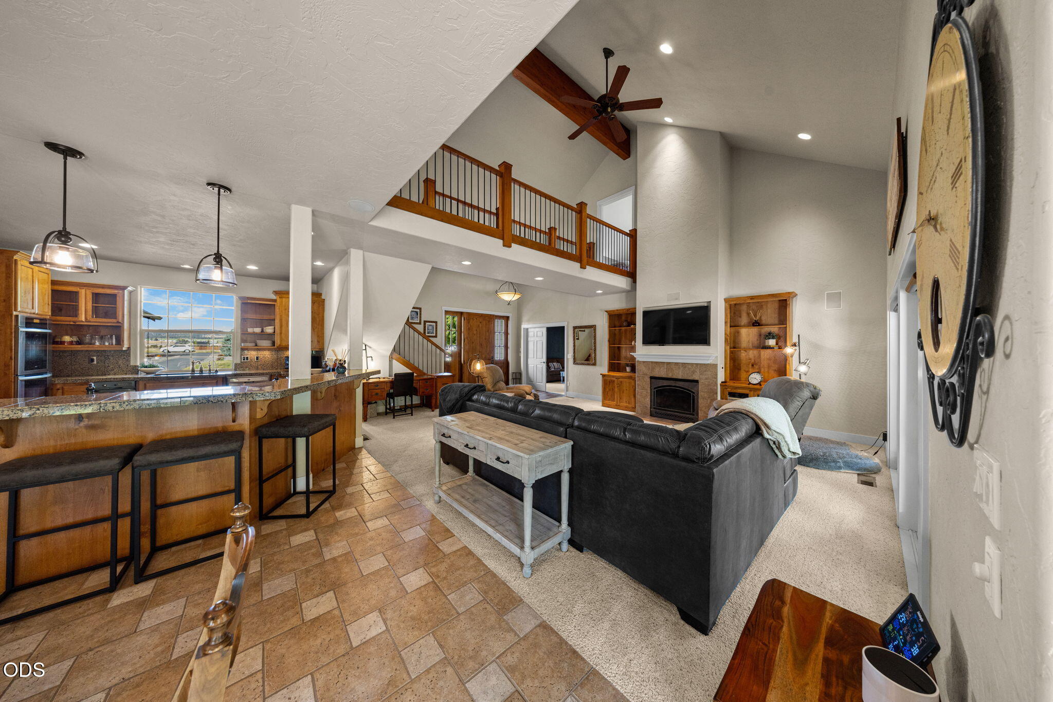 Open-plan living room and kitchen with a loft railing, vaulted ceiling, and fireplace.