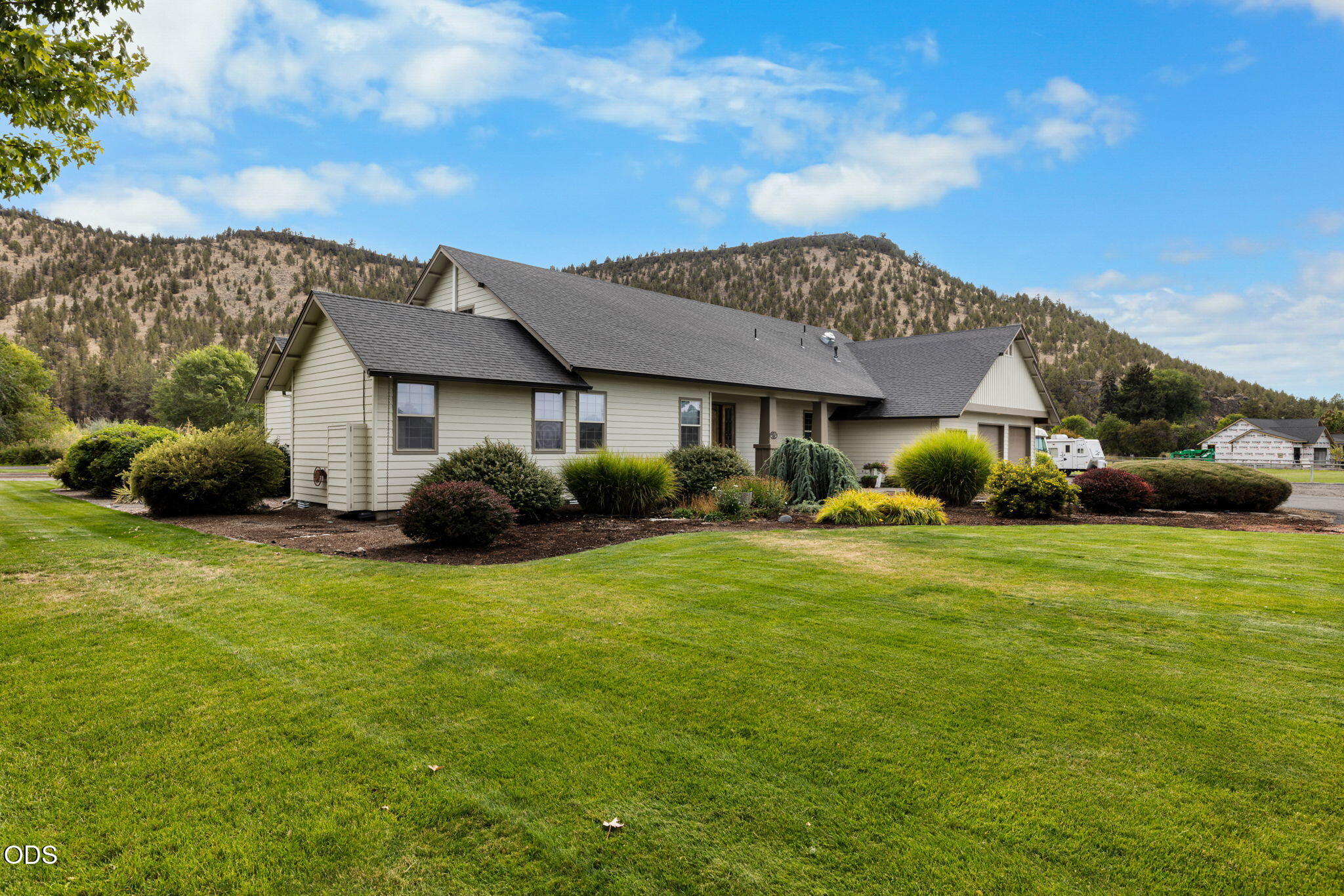 Single-story home with gabled roofs, landscaped shrubs, and a broad lawn backed by tree-covered hills.