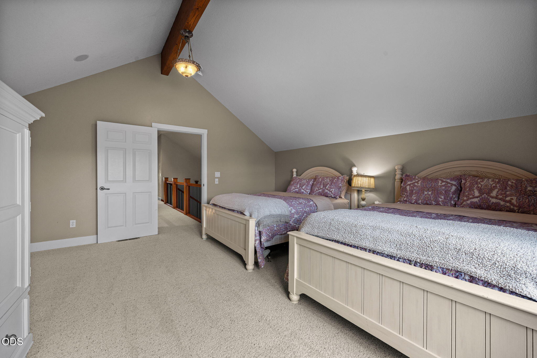 Bedroom with two beds beneath a vaulted ceiling and exposed wooden beam.