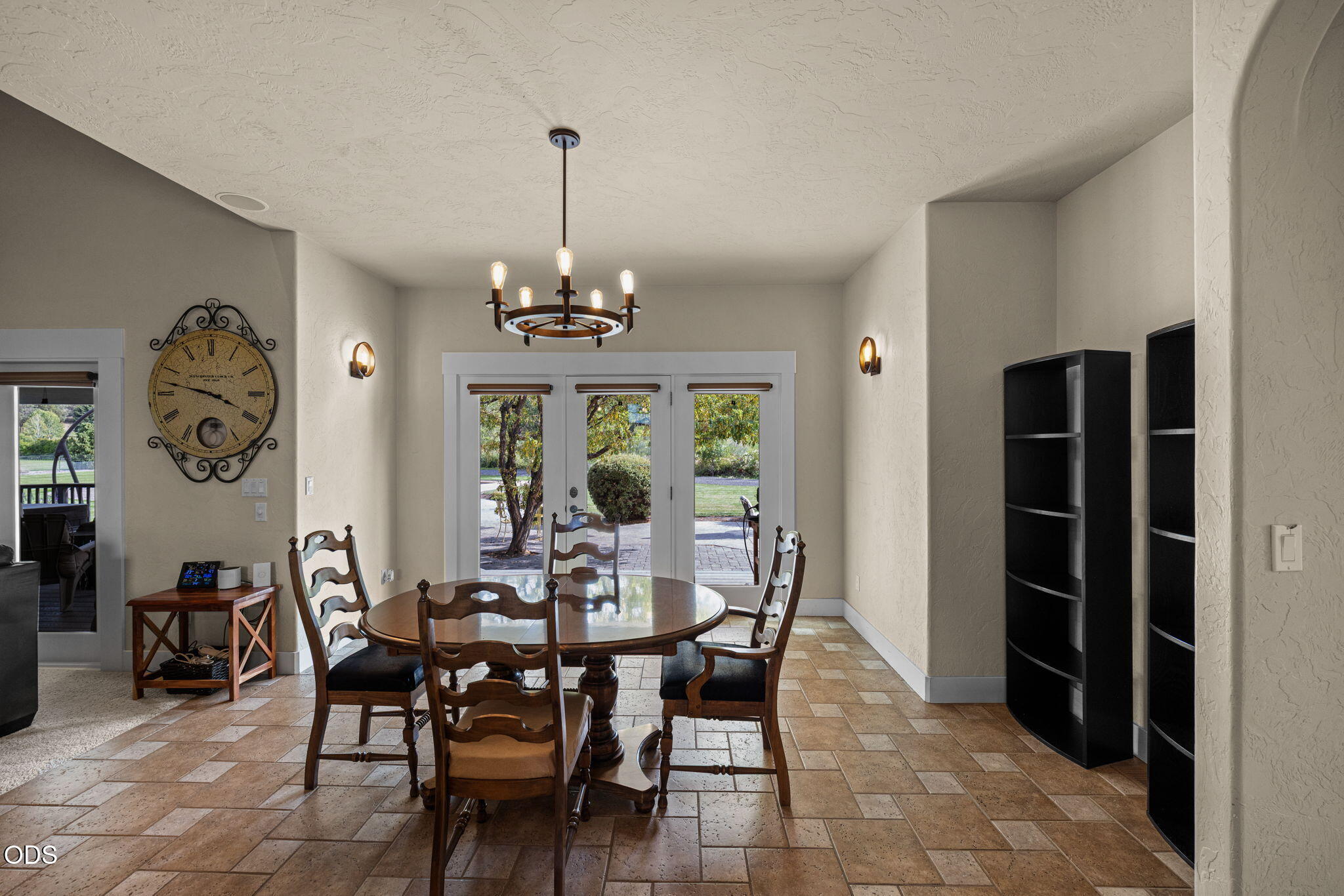 Dining room with a round wooden table, dark chandelier, and glass doors opening to a patio.