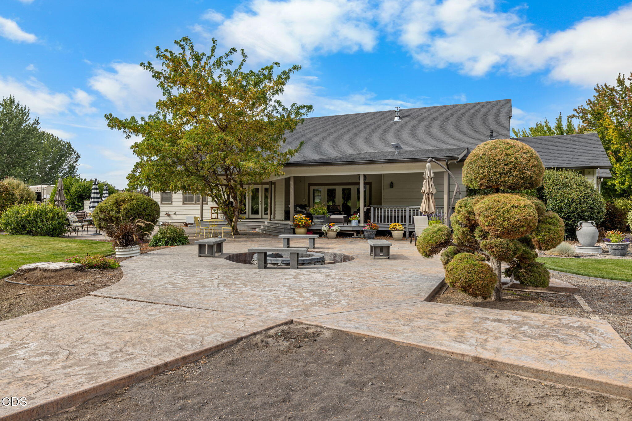 Home’s covered rear porch and landscaped patio with a circular fire pit and outdoor seating.
