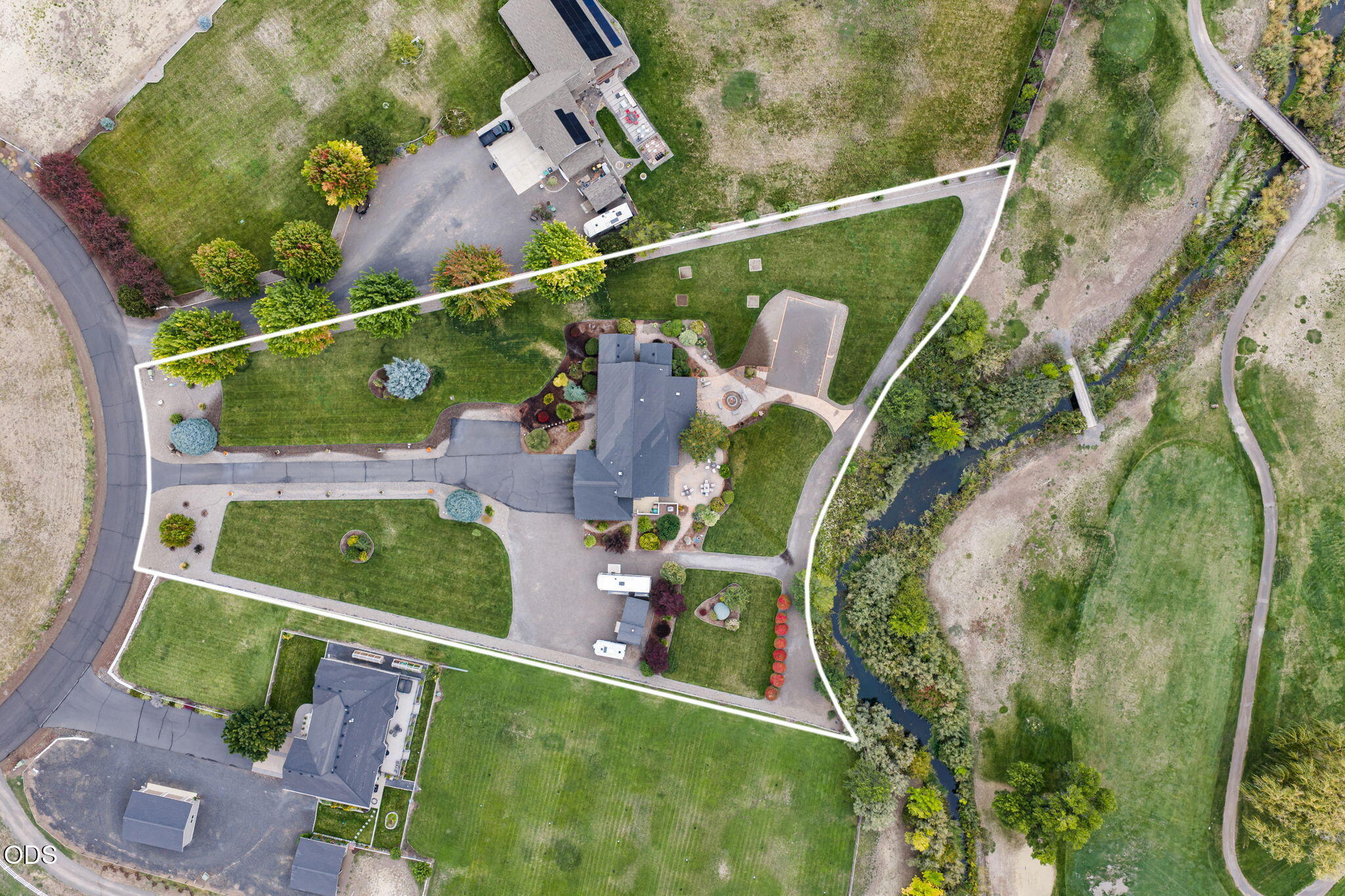 Aerial view of a landscaped home and grounds beside a tree-lined creek, outlined in white.