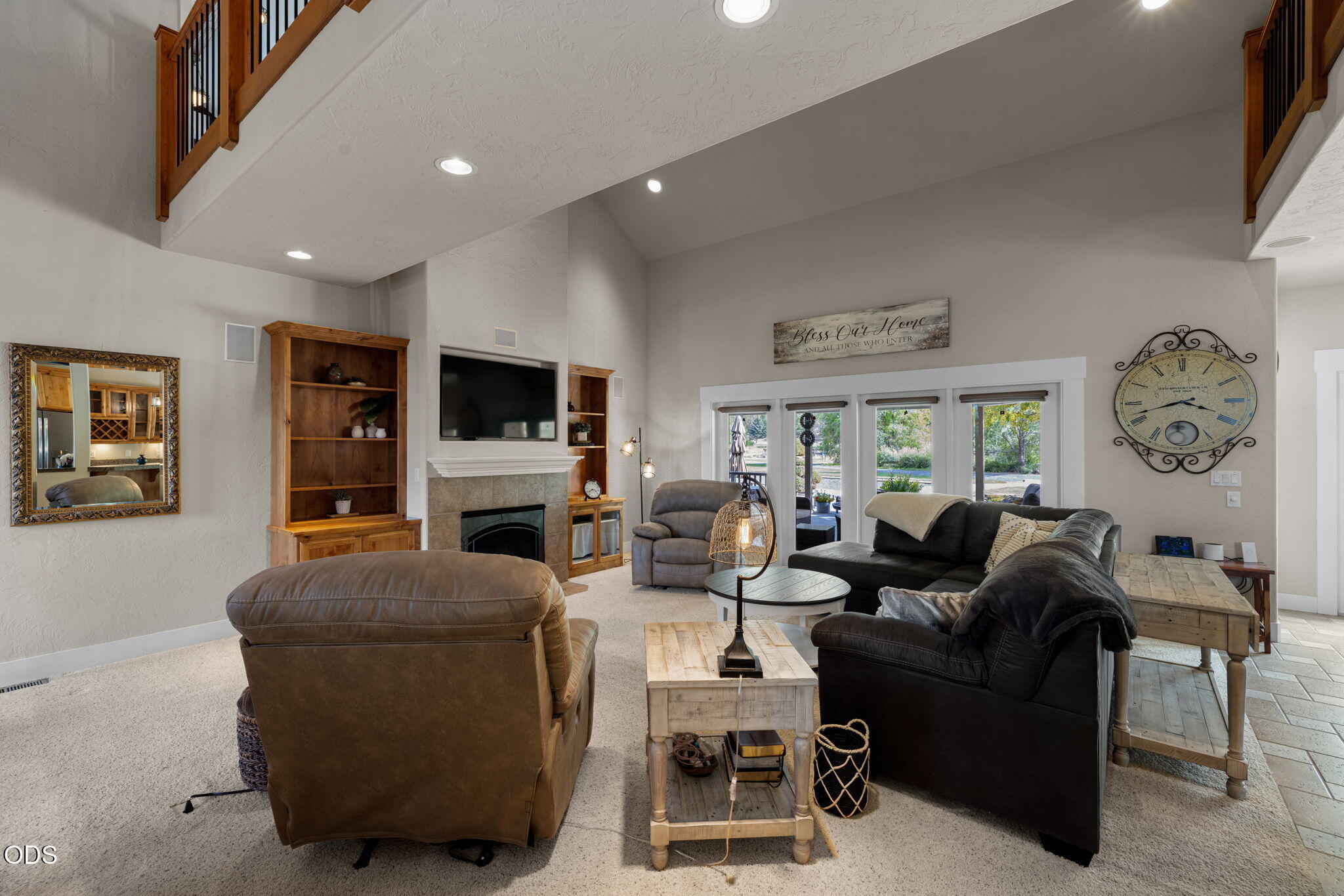 Furnished living room with vaulted ceiling, stone fireplace, built-in shelves, and large garden-facing windows.