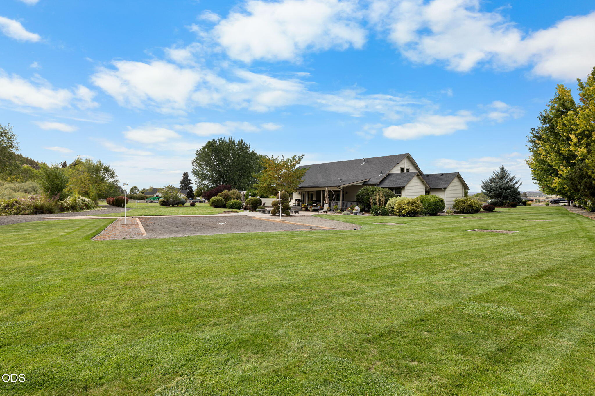 Home with a covered porch, broad lawn, landscaped garden, and gravel recreation area.