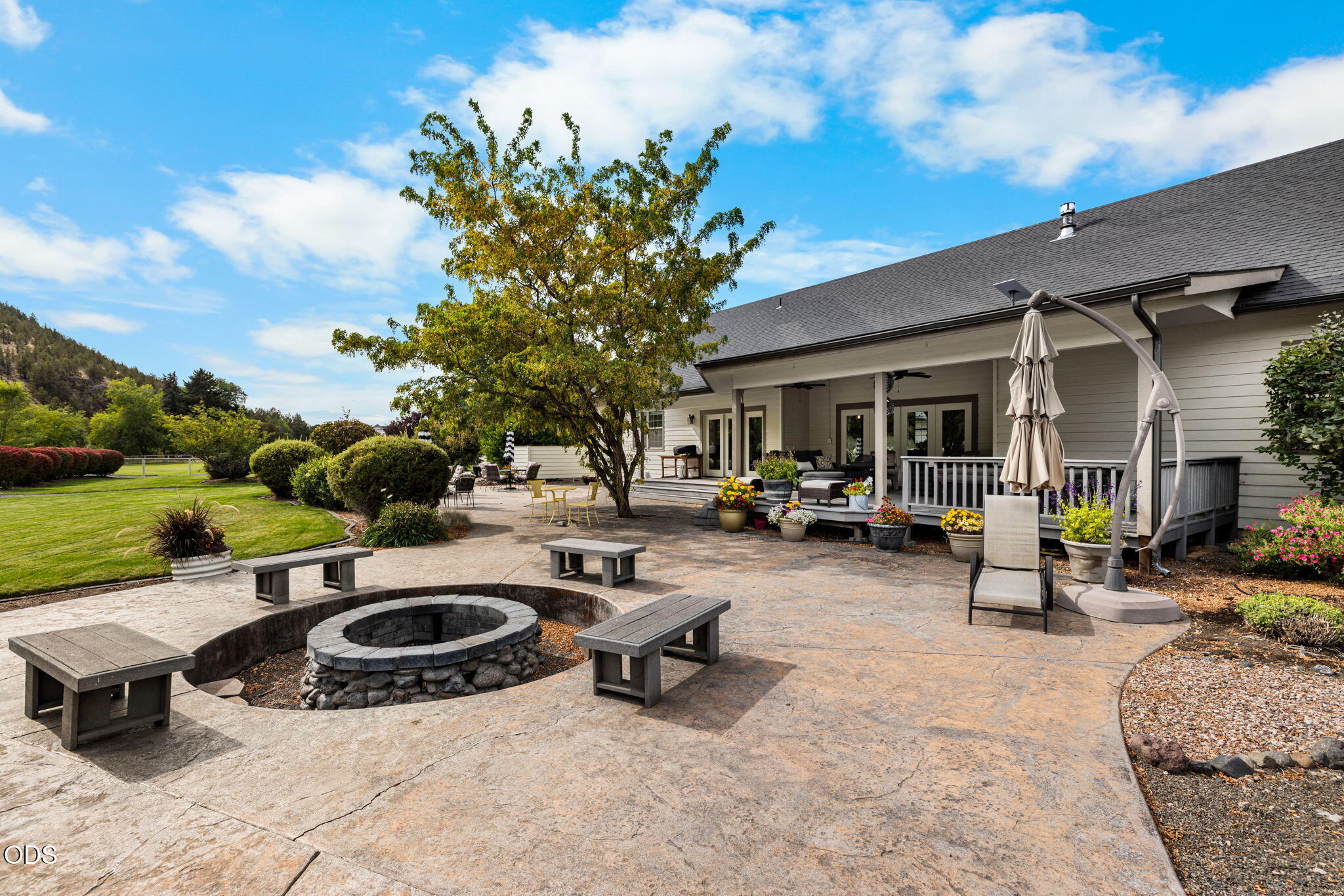 Back patio with circular stone fire pit, outdoor seating, covered porch, and landscaped lawn.