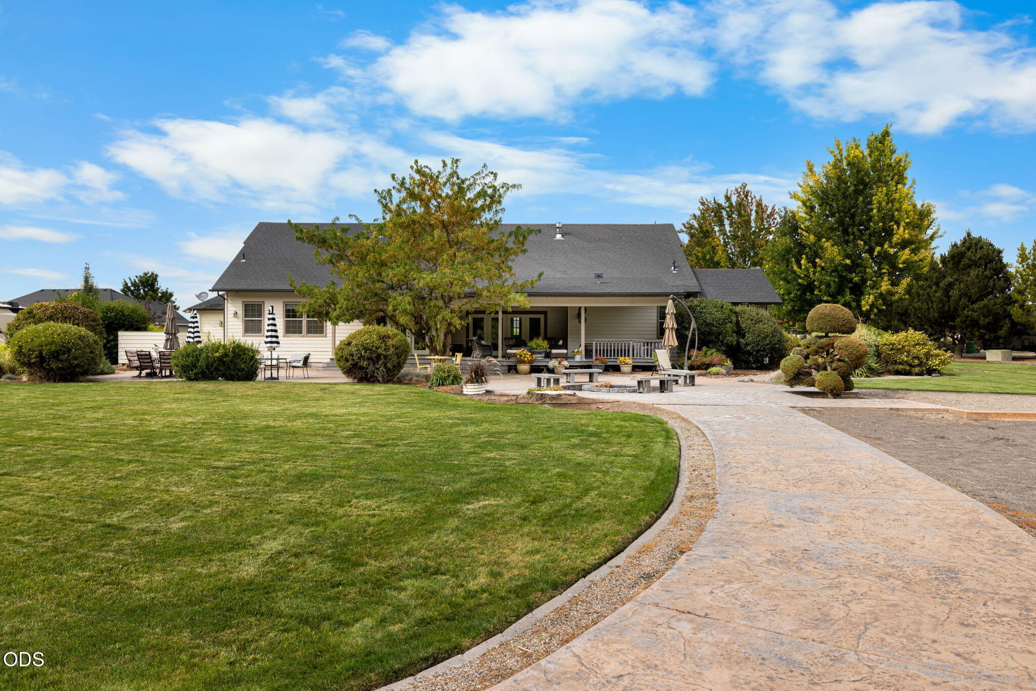 Home’s rear exterior with a covered patio, landscaped lawn, mature trees, and a curved paved driveway.