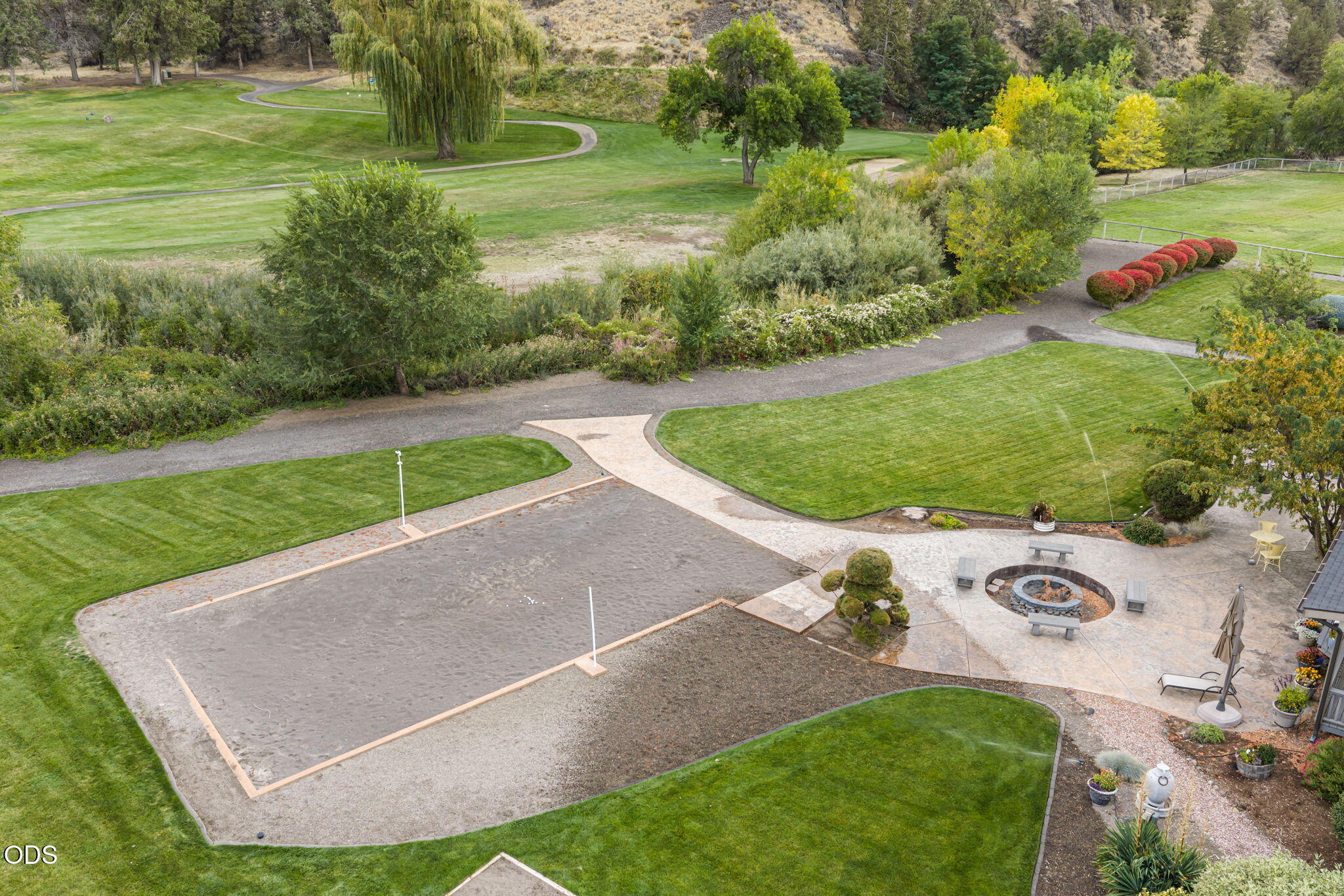 Landscaped grounds with a bocce court, winding paths, and a circular fire pit patio.