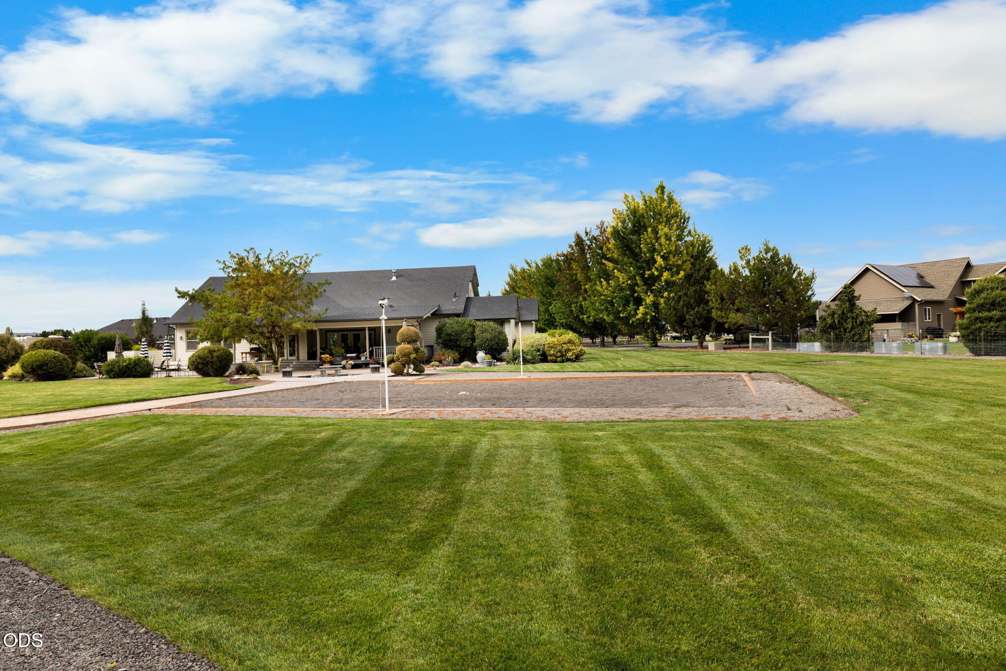 Rear of a home beyond a broad lawn, landscaped patio, and rectangular gravel recreation area.