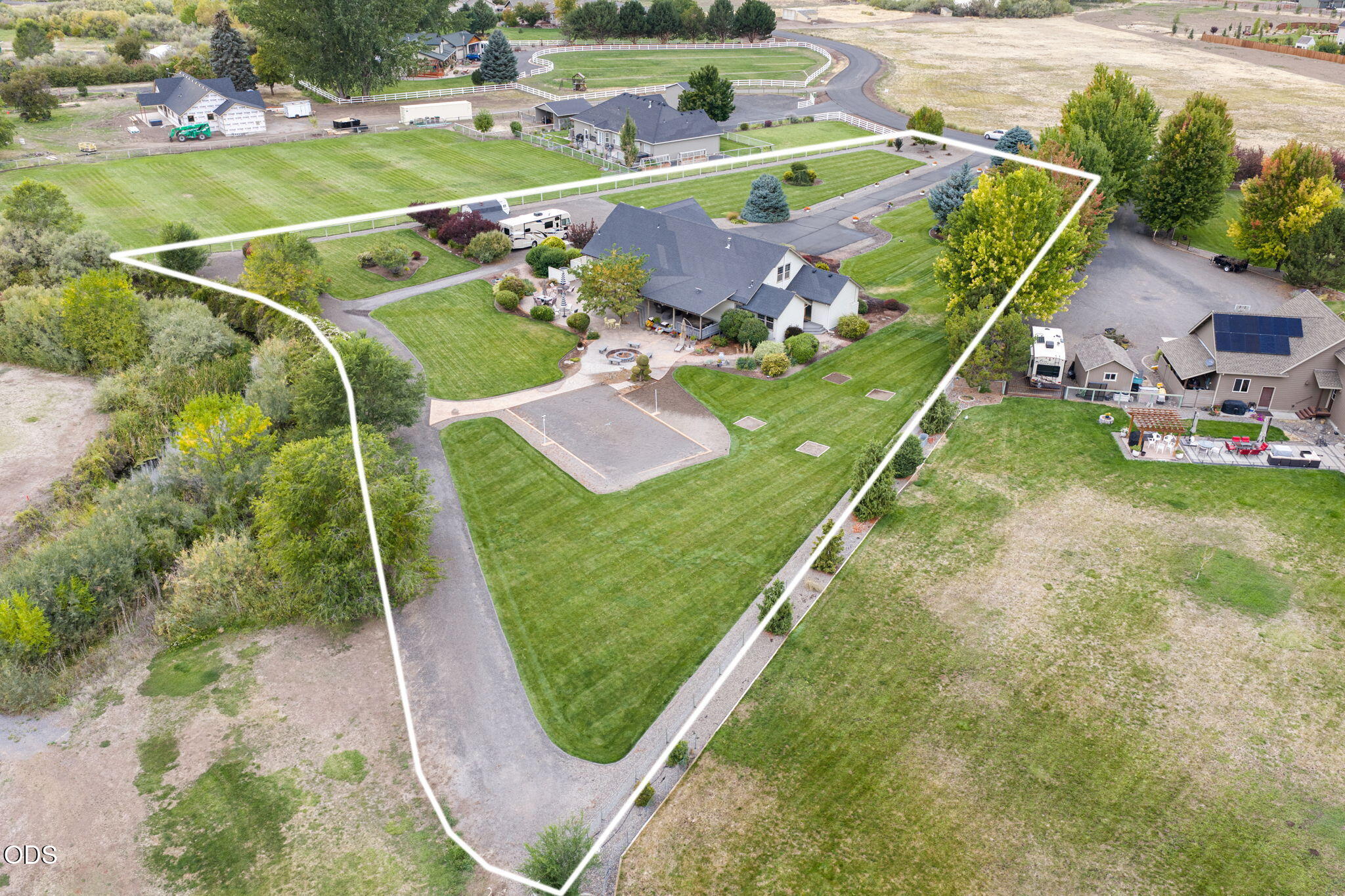 Aerial view of a house and landscaped lot outlined in white, with a paved drive and fire pit.