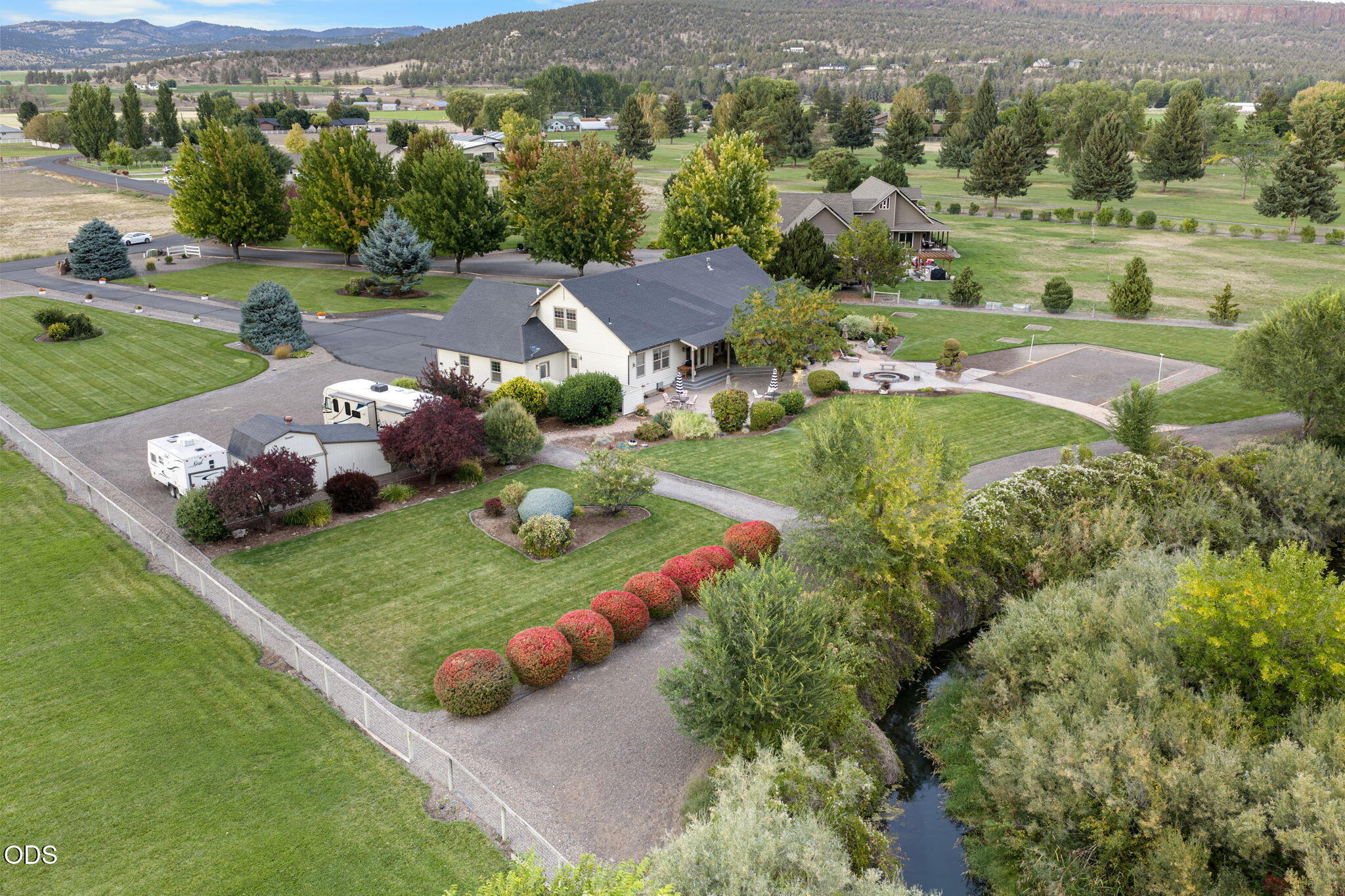 Aerial view of a landscaped home beside a creek, with broad lawns and recreational vehicles.