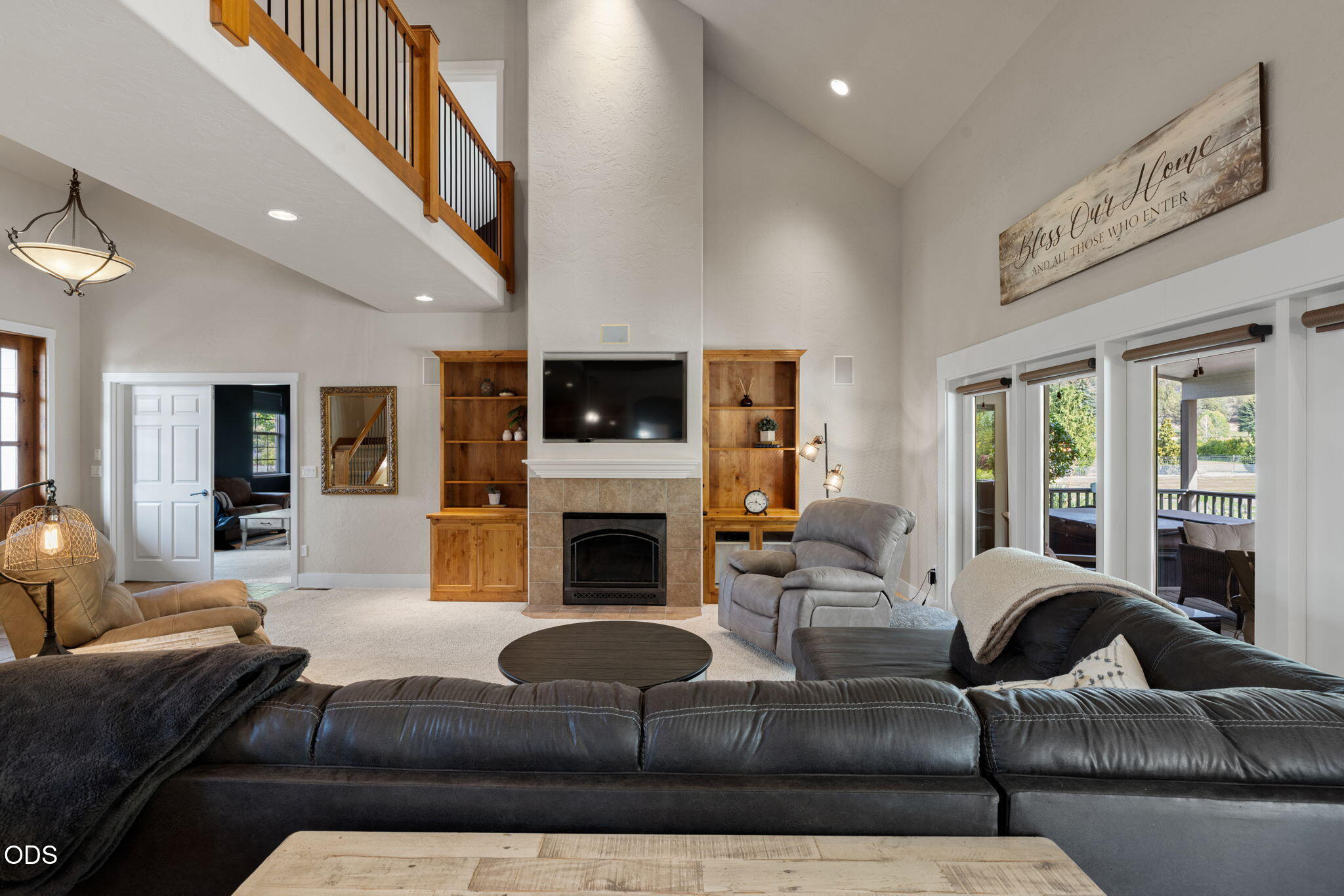 Living room with a vaulted ceiling, stone fireplace, wood built-ins, and sliding doors to a covered deck.