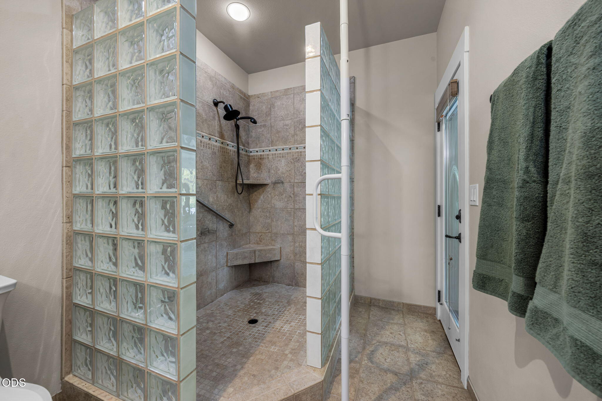 Walk-in tiled shower with glass-block partitions, a built-in bench, grab bars, and green towels.