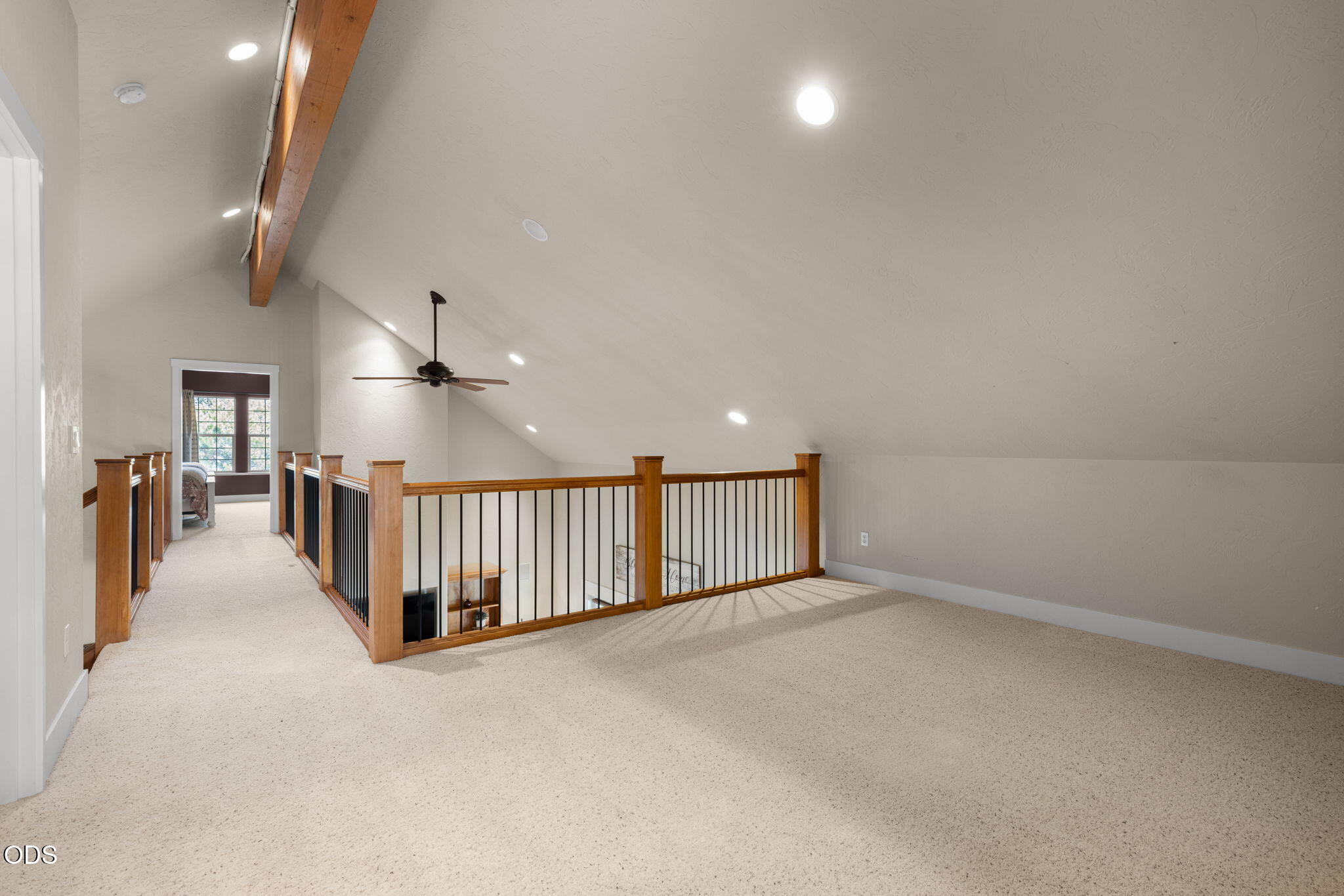 Carpeted loft landing with a vaulted ceiling, exposed wood beam, and railing overlooking the lower level.
