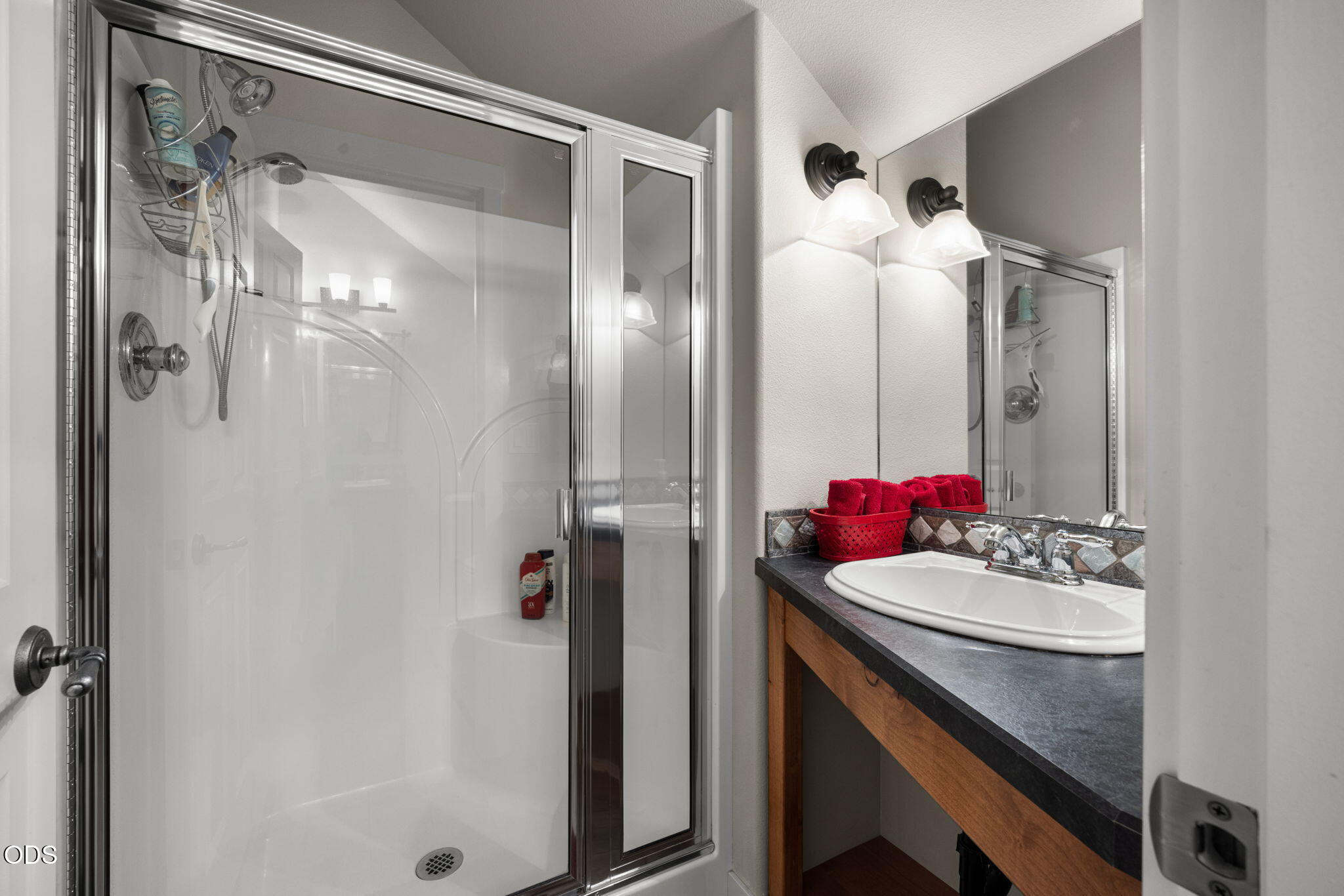 Bathroom with a glass-enclosed shower and wood vanity topped with red towels.