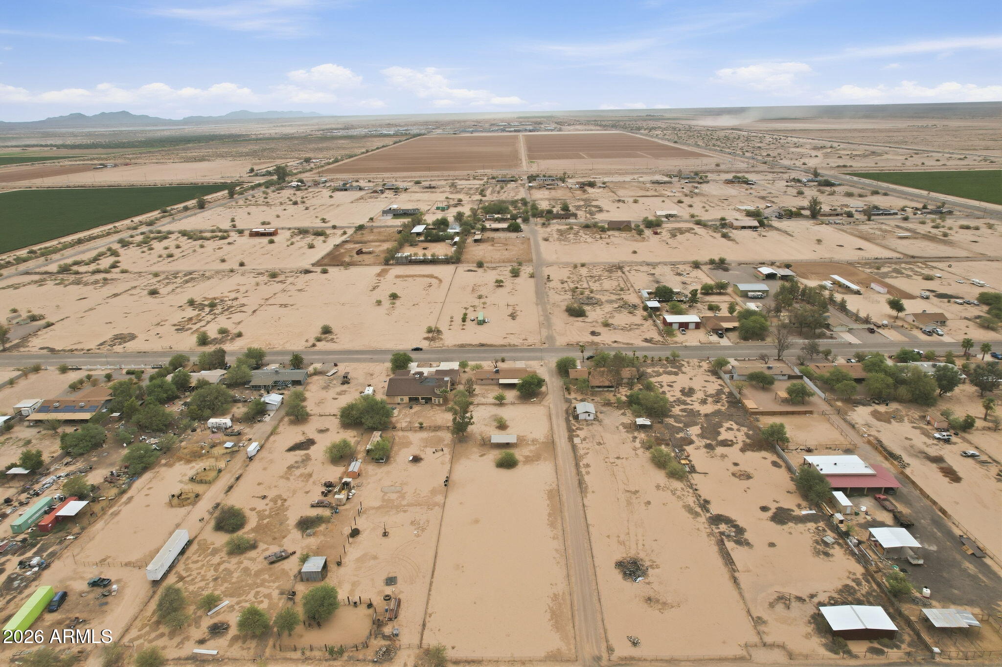 Aerial view of sandy rural acreage with outbuildings, neighboring parcels, fields, and distant mountains.