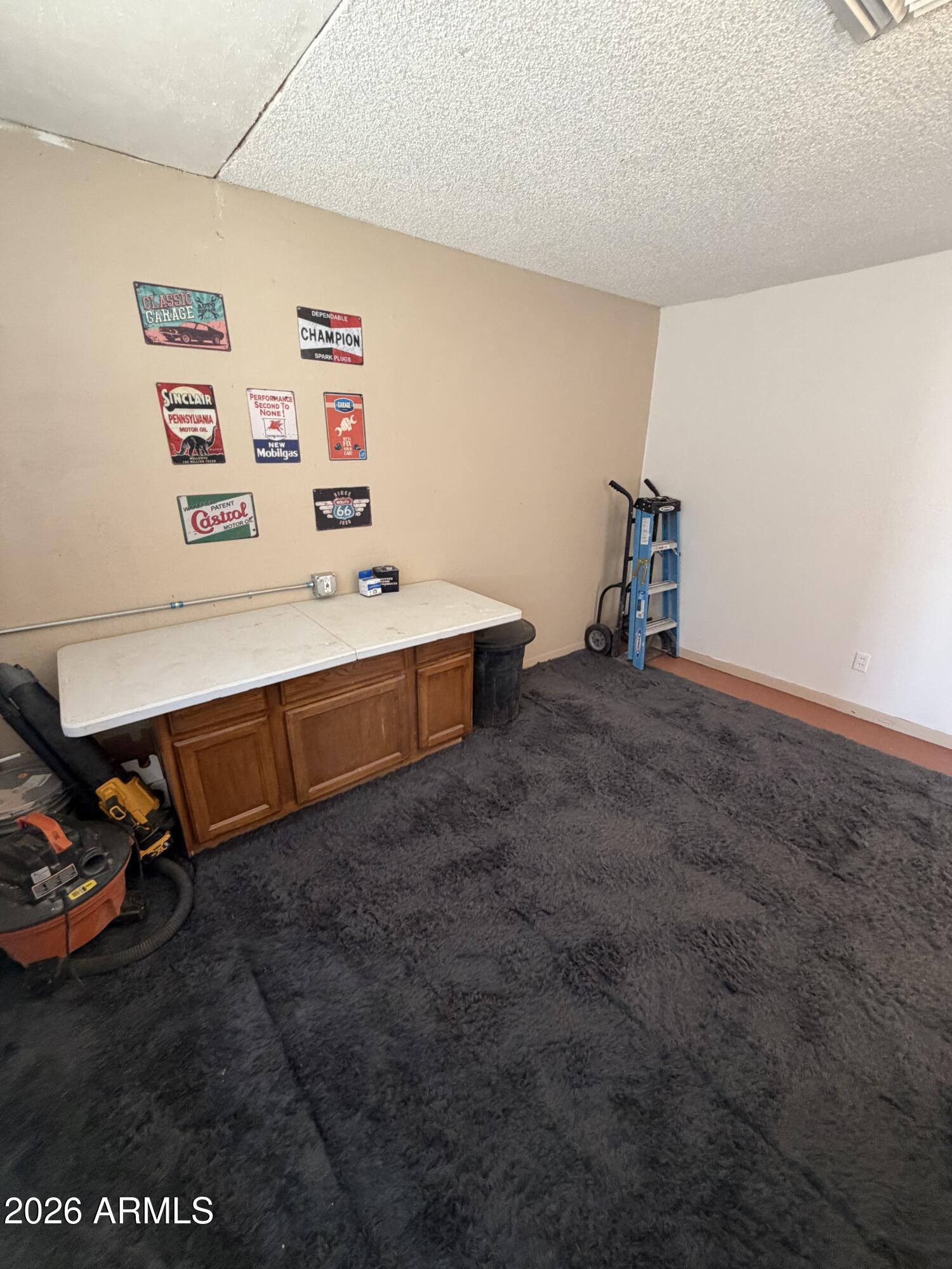 Carpeted garage workshop with a cabinet workbench, vintage automotive signs, and a blue hand truck.