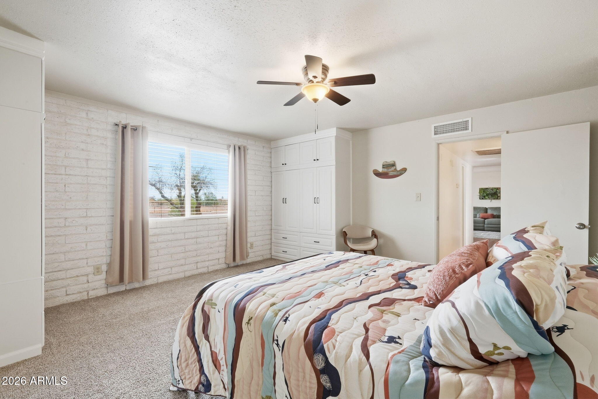 Furnished bedroom with colorful bedding, white built-in wardrobes, and a white brick wall.