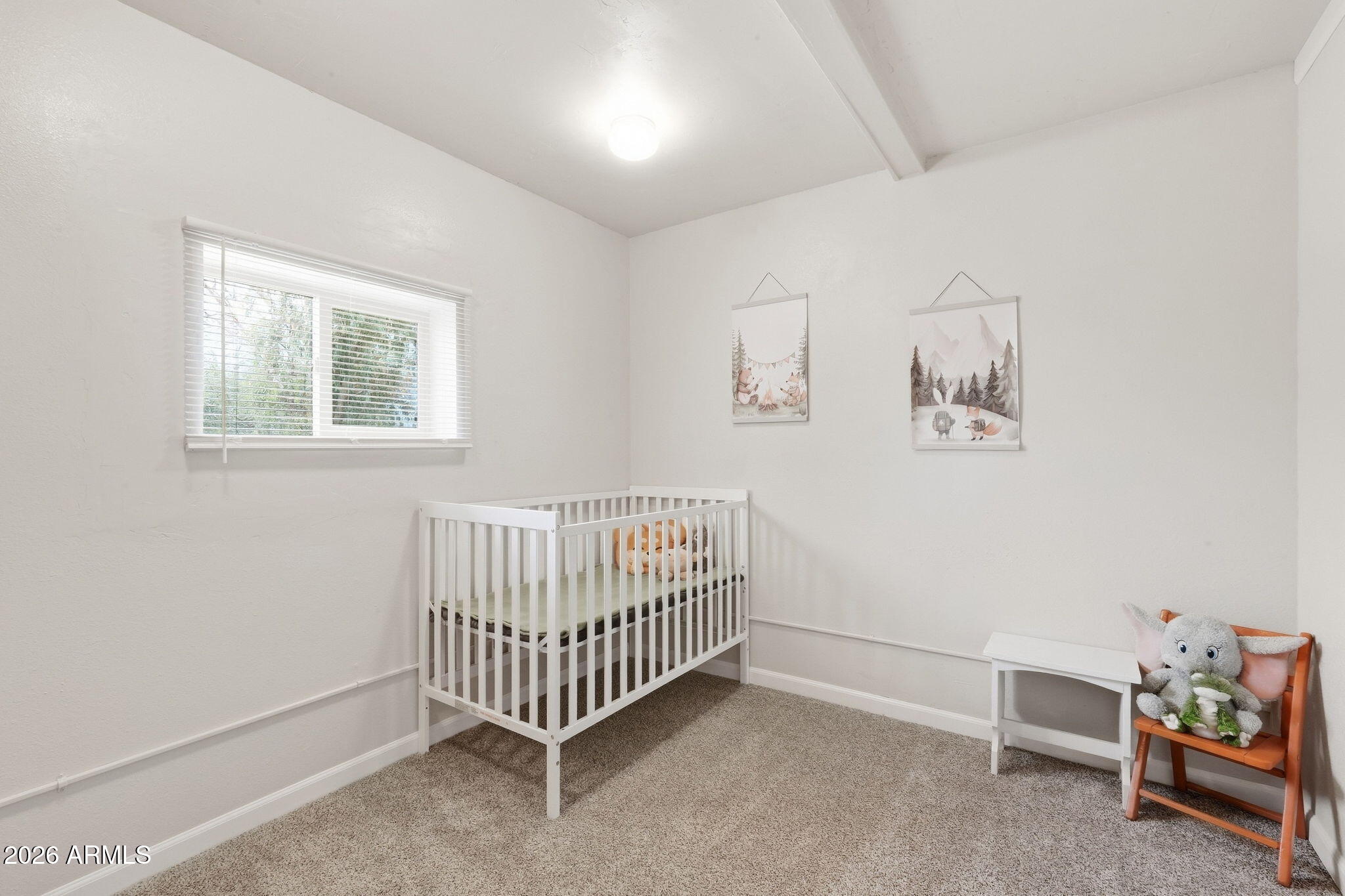 Nursery with a white crib, woodland prints, and a stuffed elephant on a small chair.
