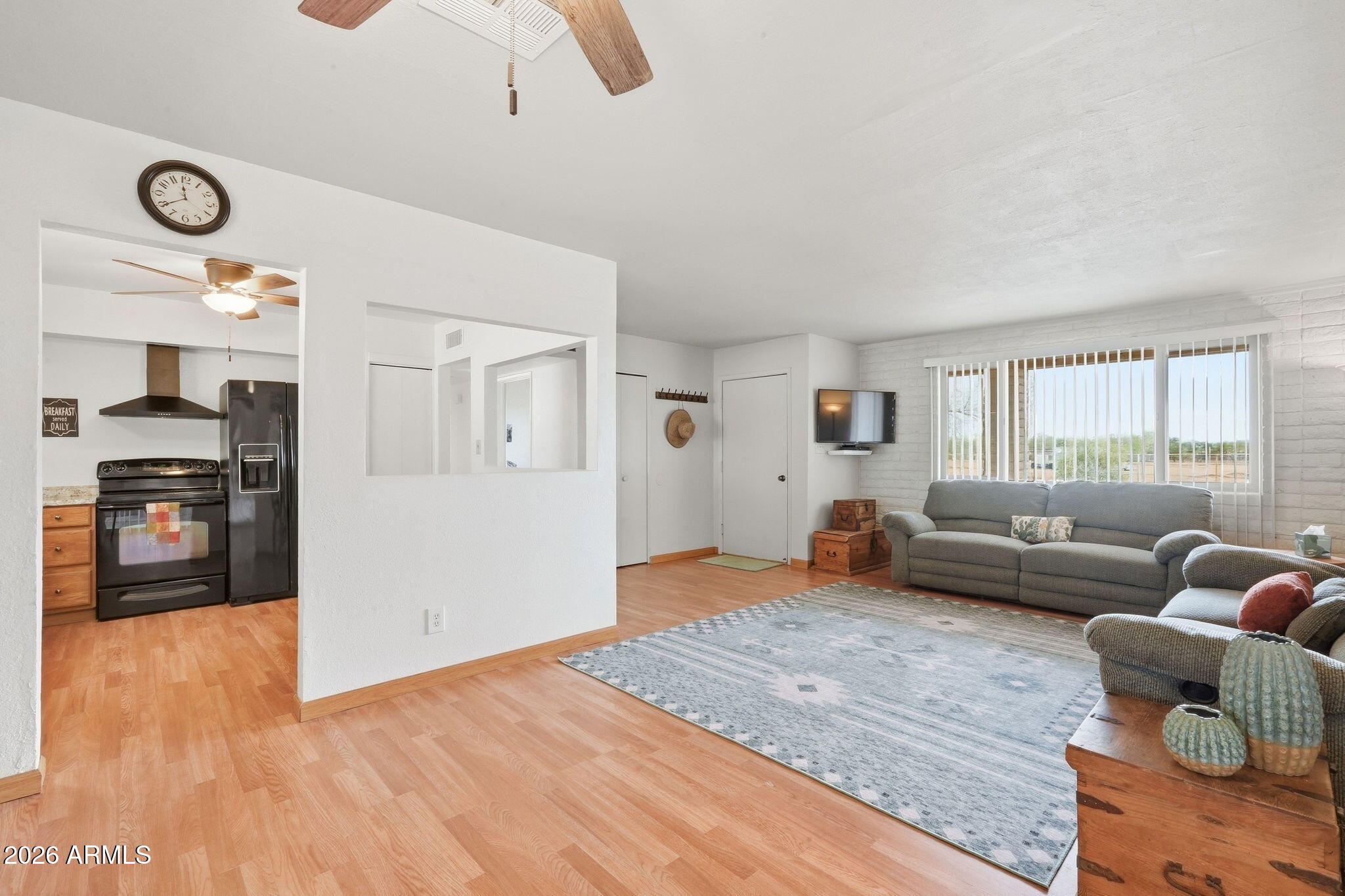 Open-plan living room and kitchen with a gray sofa, patterned rug, and black kitchen appliances.