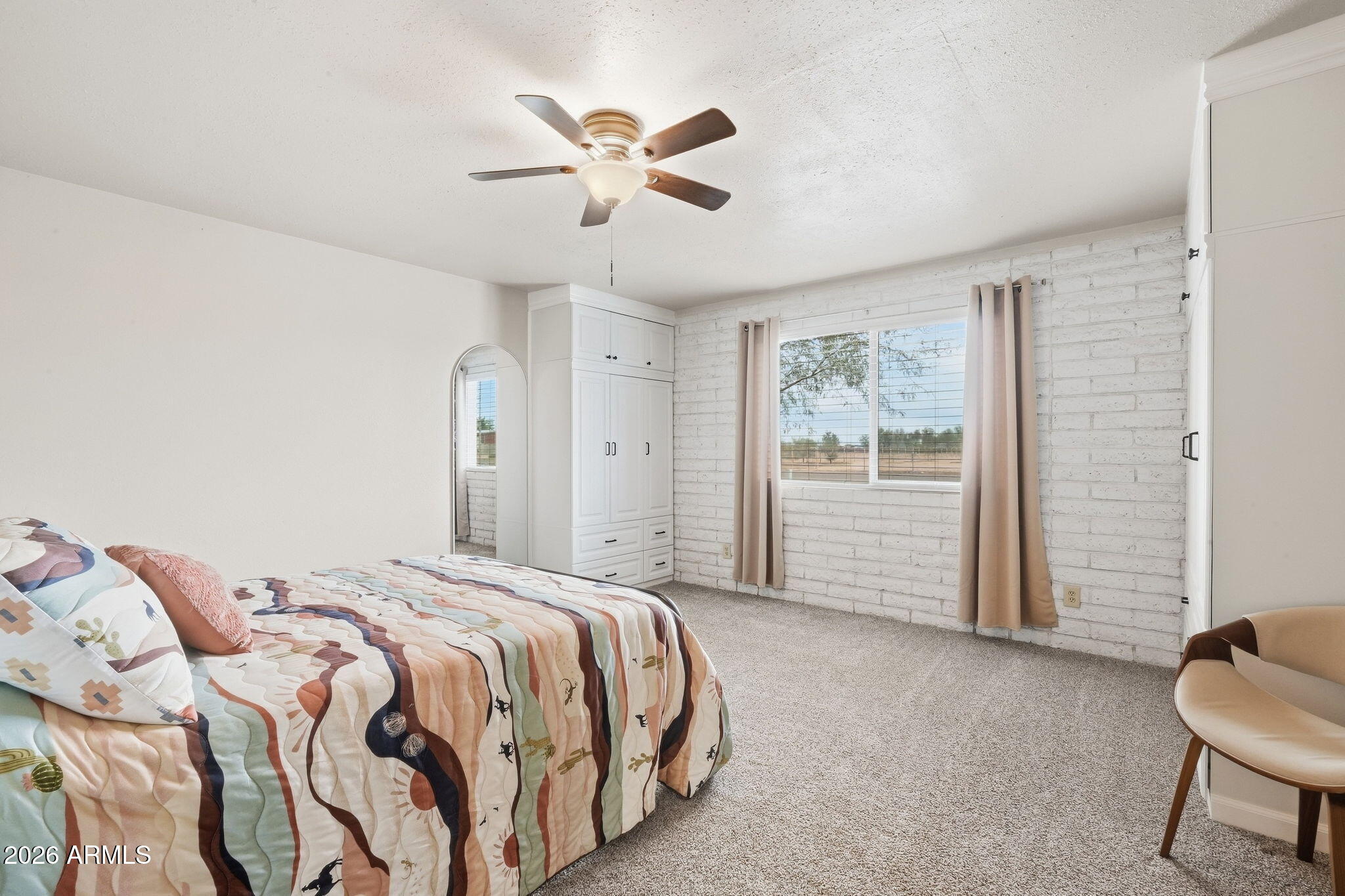 Furnished bedroom with white brick walls, built-in wardrobes, and a window overlooking a rural landscape.