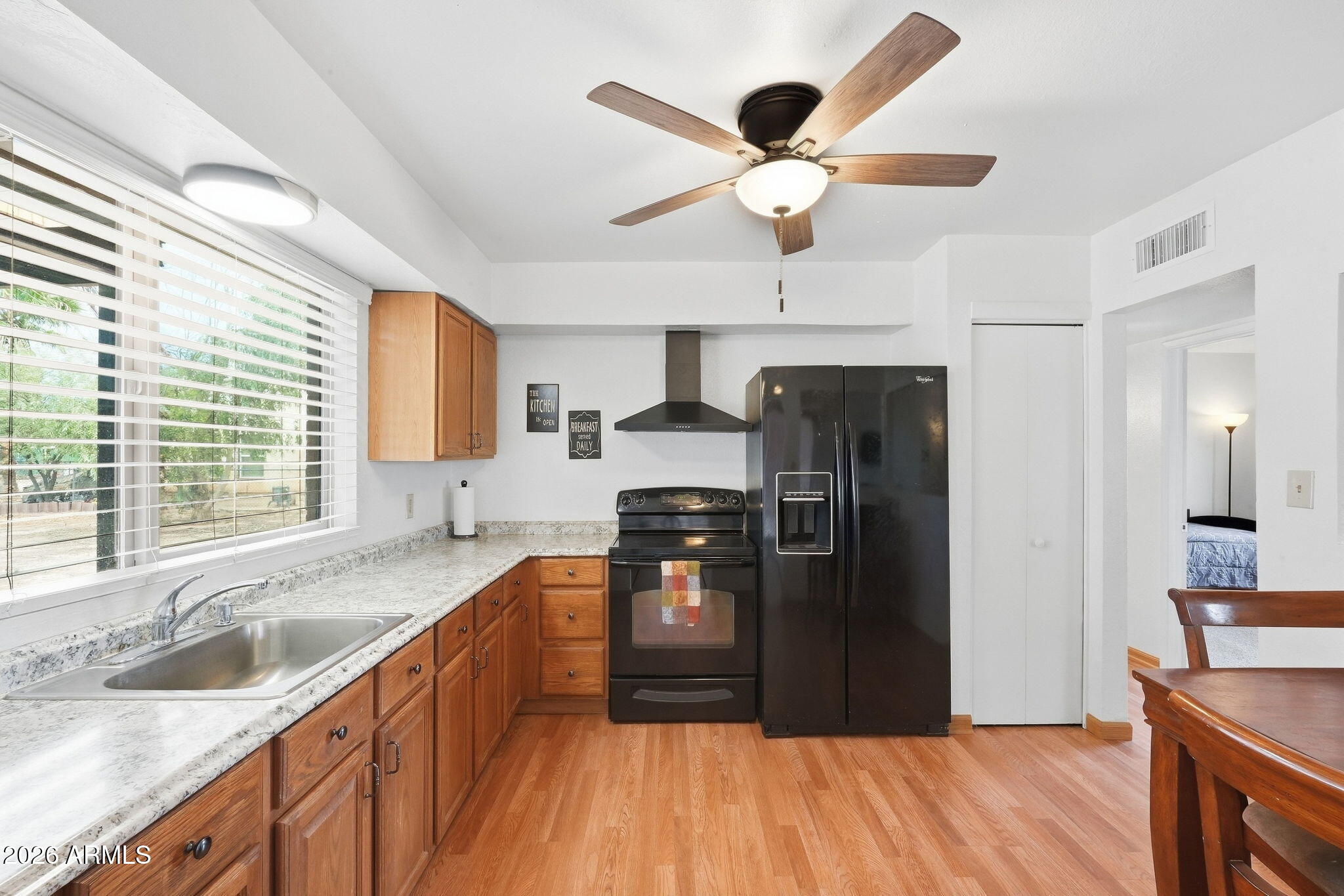Kitchen with wood cabinets, stone countertops, black appliances, and a large window overlooking trees.