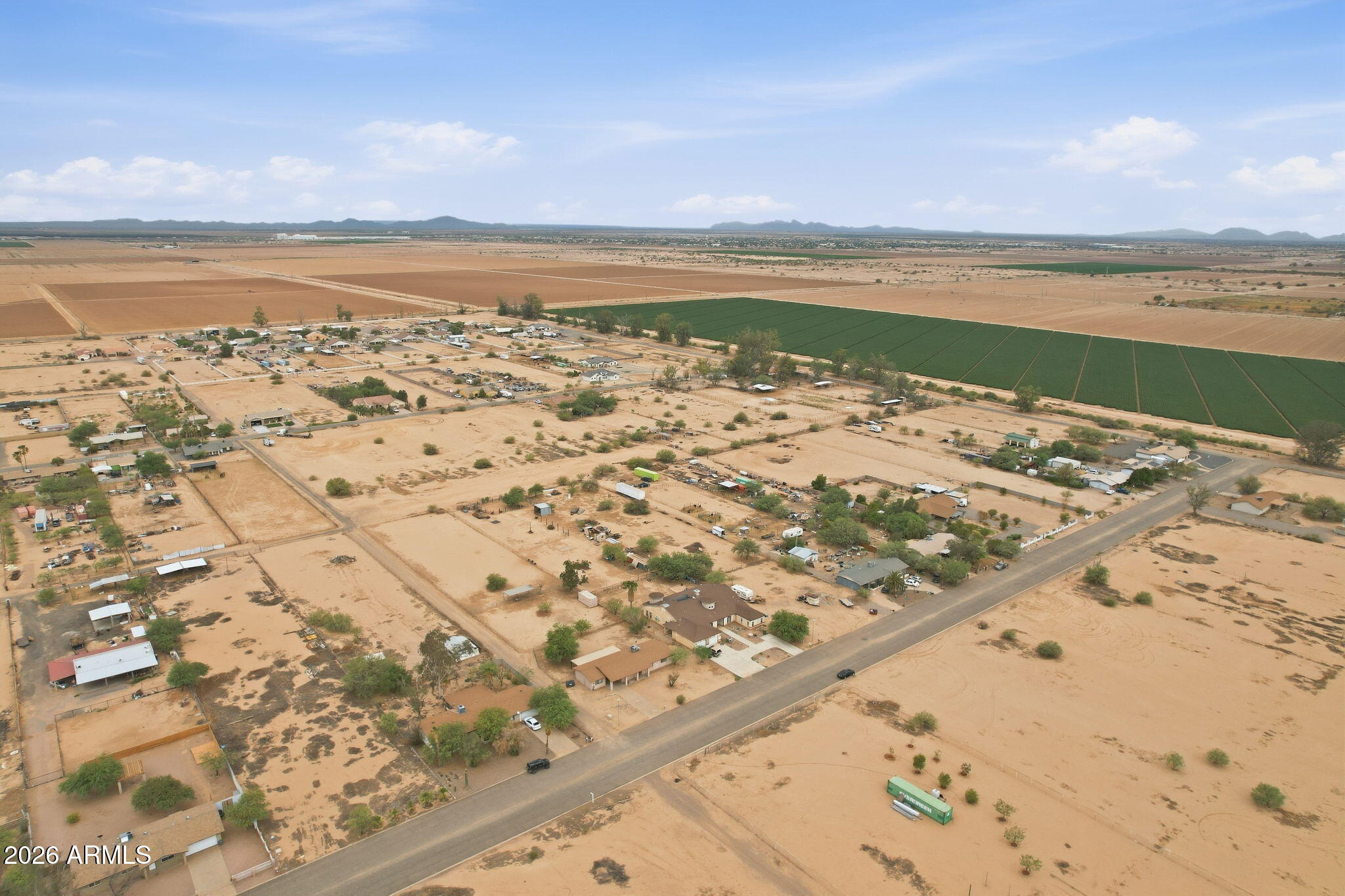 Aerial view of desert homes and agricultural fields beside a paved road.