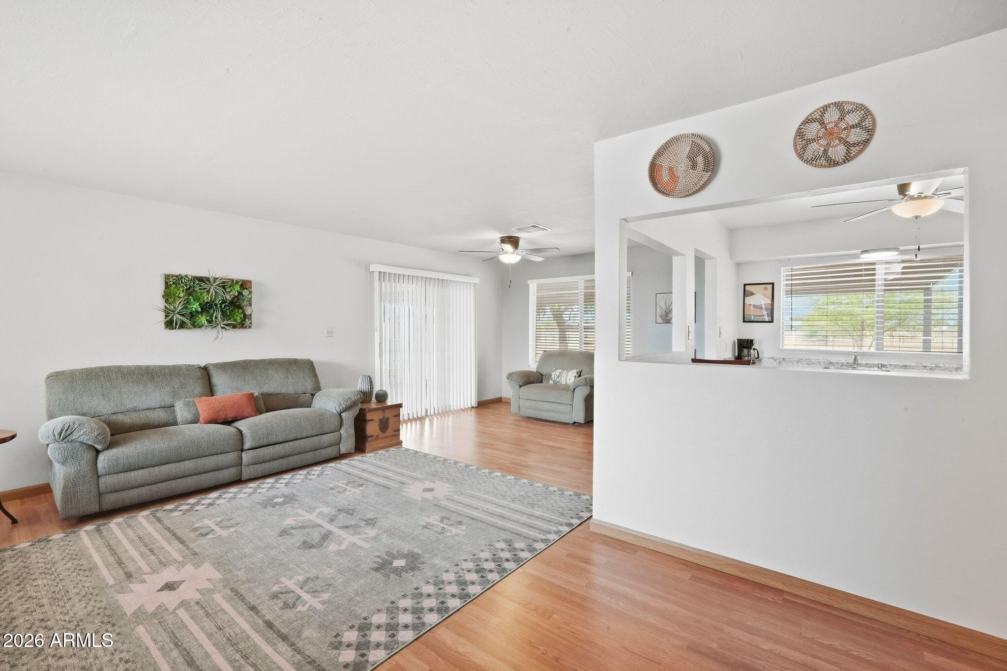 Living room with gray sofas, a patterned rug, wood floors, and a kitchen pass-through.