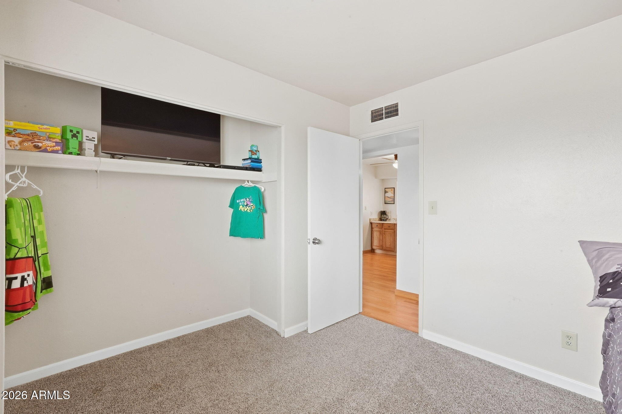 Bedroom with an open built-in closet, television on a shelf, and doorway to a wood-floored hall.