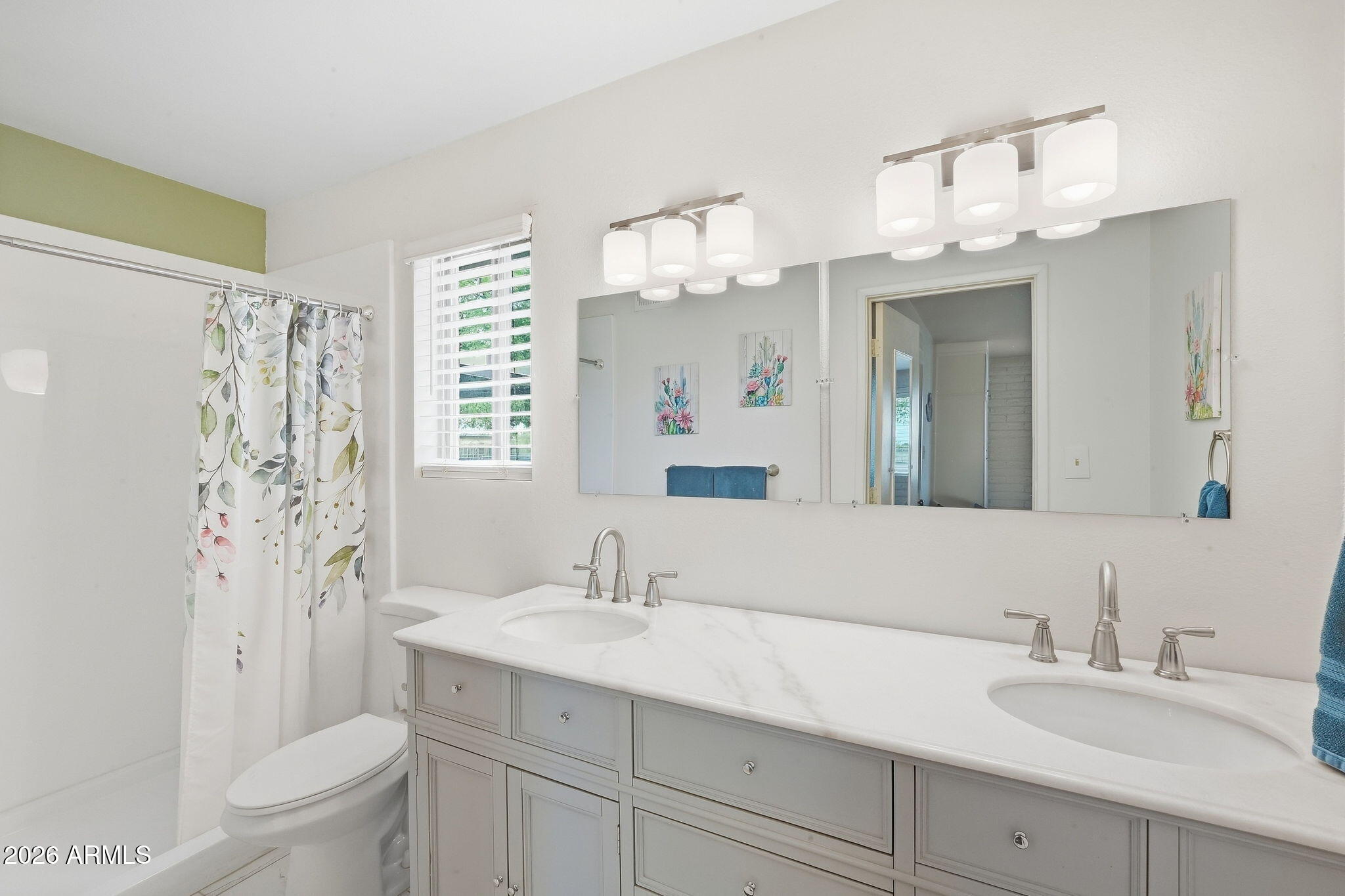 Bathroom with a gray double vanity, broad mirrors, and a shower with a floral curtain.