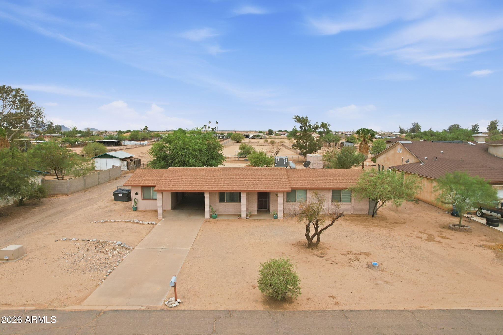 Aerial view of a single-story home with a wide sandy yard, scattered trees, and concrete driveway.