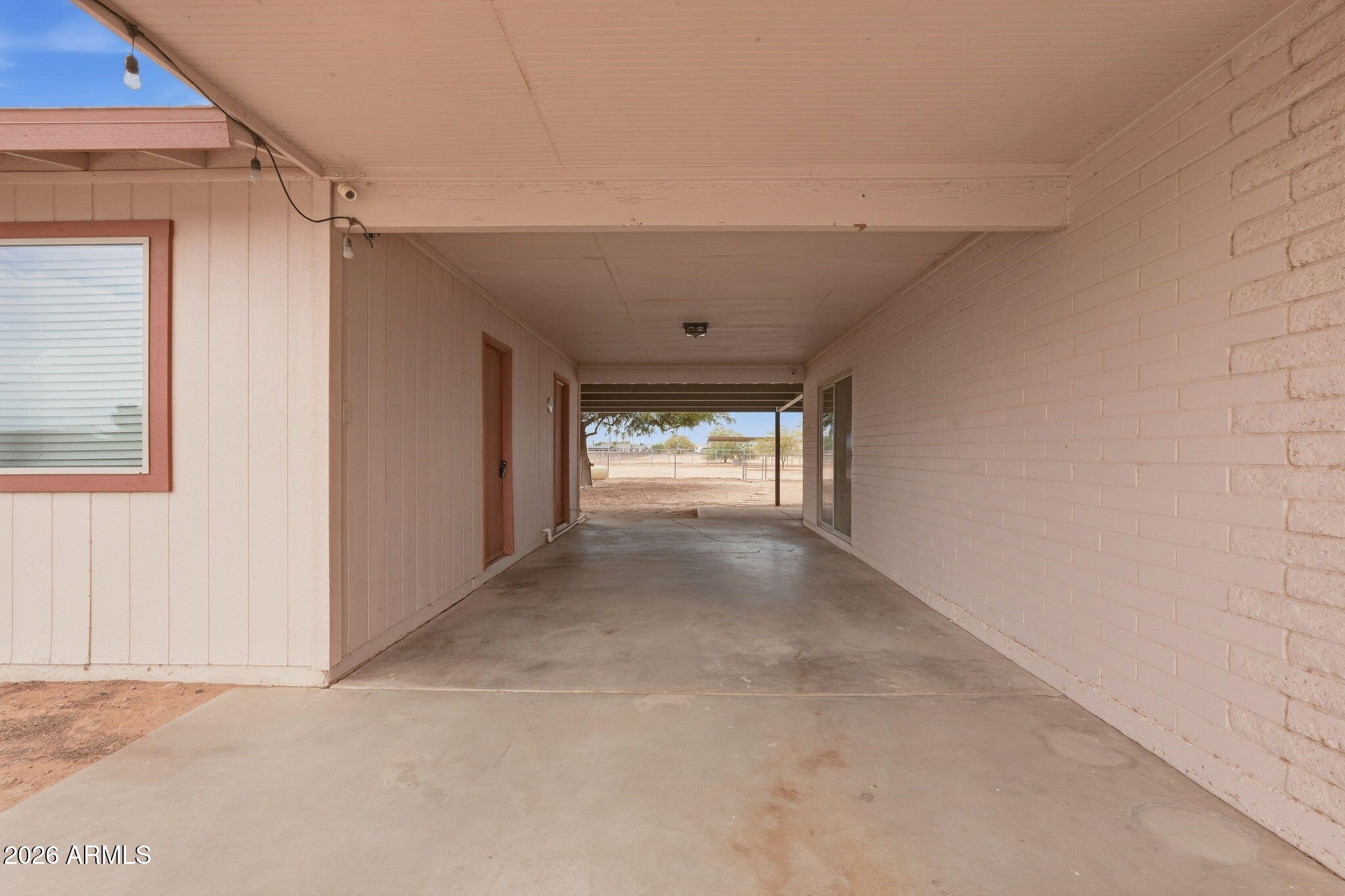 Covered concrete patio beside the home, opening onto a fenced yard.