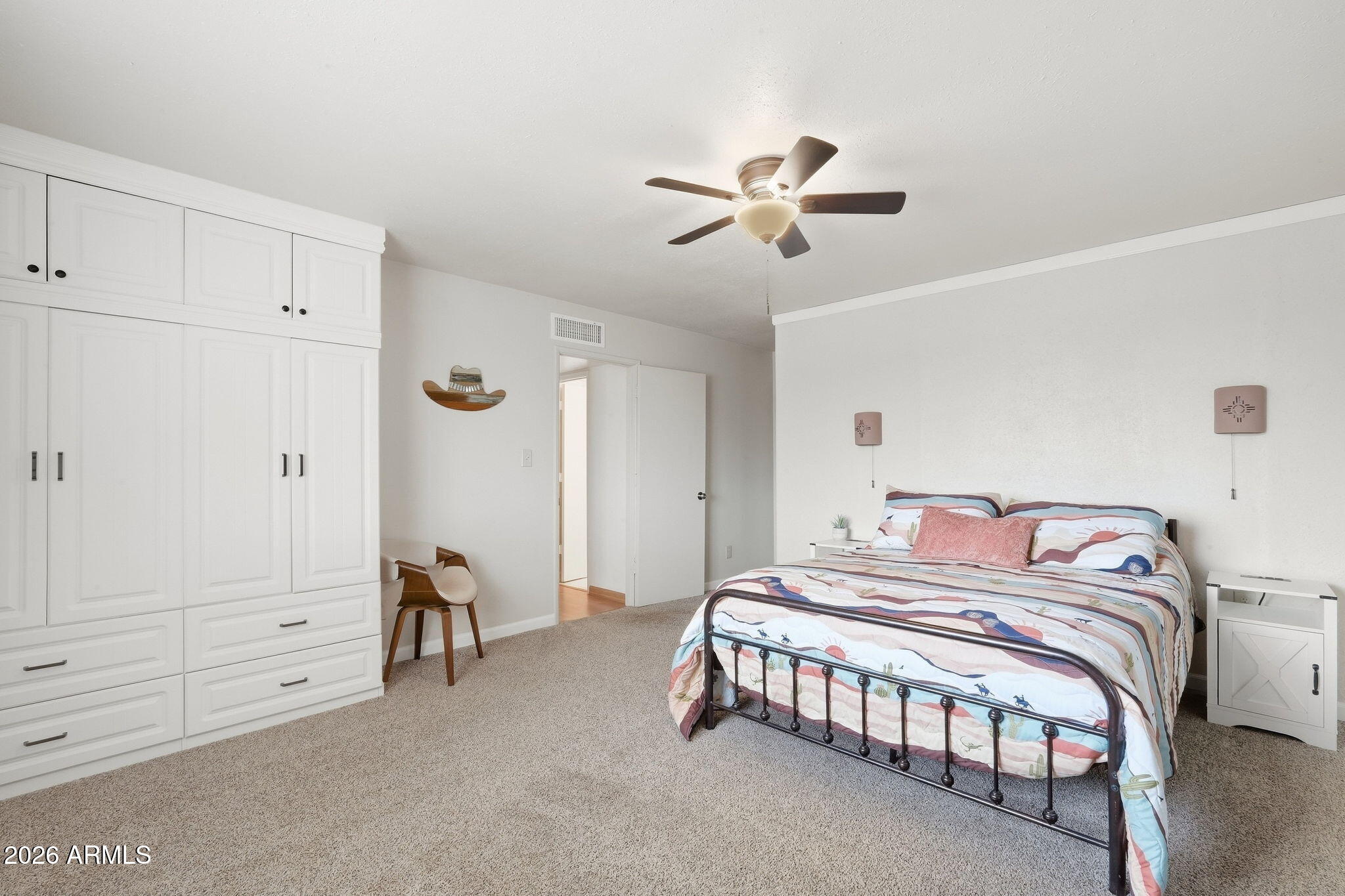 Bedroom with colorful striped bedding, built-in white wardrobes, carpet, and a ceiling fan.
