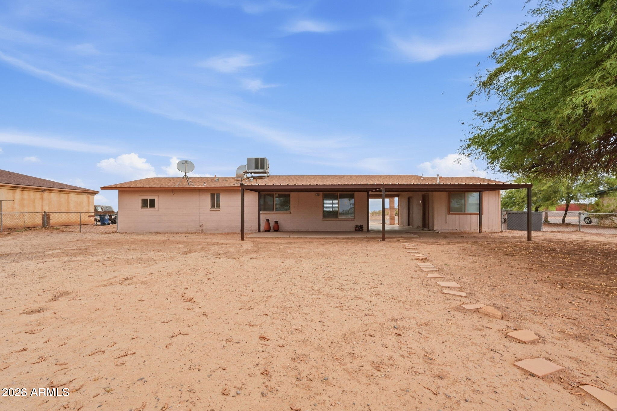 Single-story home with a long covered patio facing a broad dirt yard and stepping-stone path.